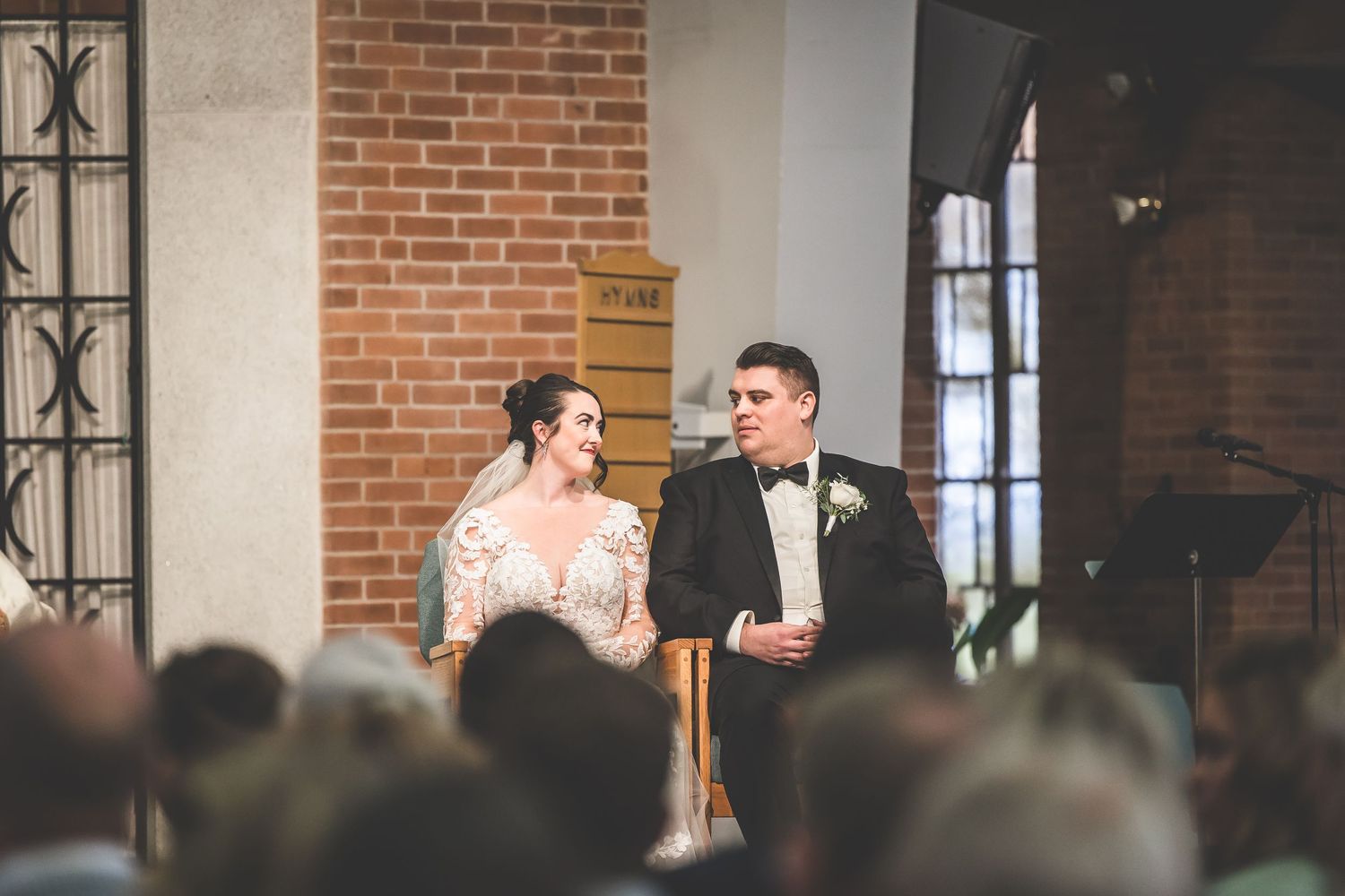 Wedding ceremony in progress inside a brick-walled church with ornate iron windows.