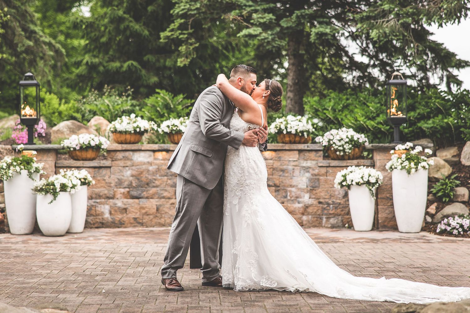 Wedding couple poses for romantic photos near stone wall with white floral decorations.