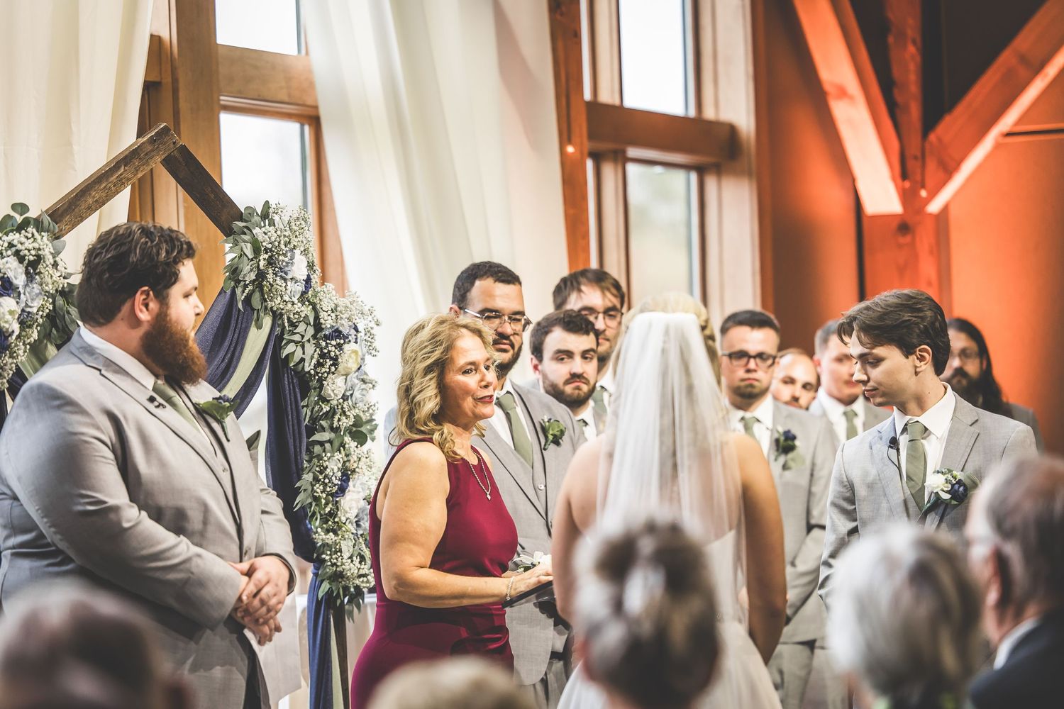 Wedding ceremony in progress at an industrial-chic venue with white drapes and wooden architecture.