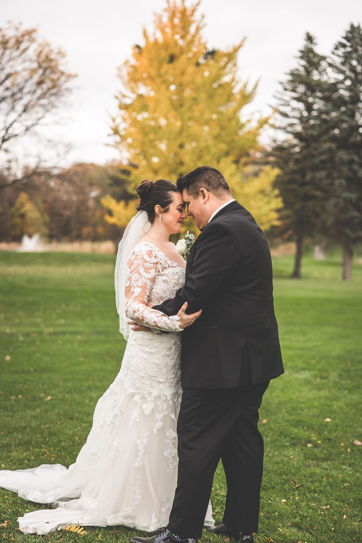 Intimate wedding moments shared between couple on grass with golden autumn trees.