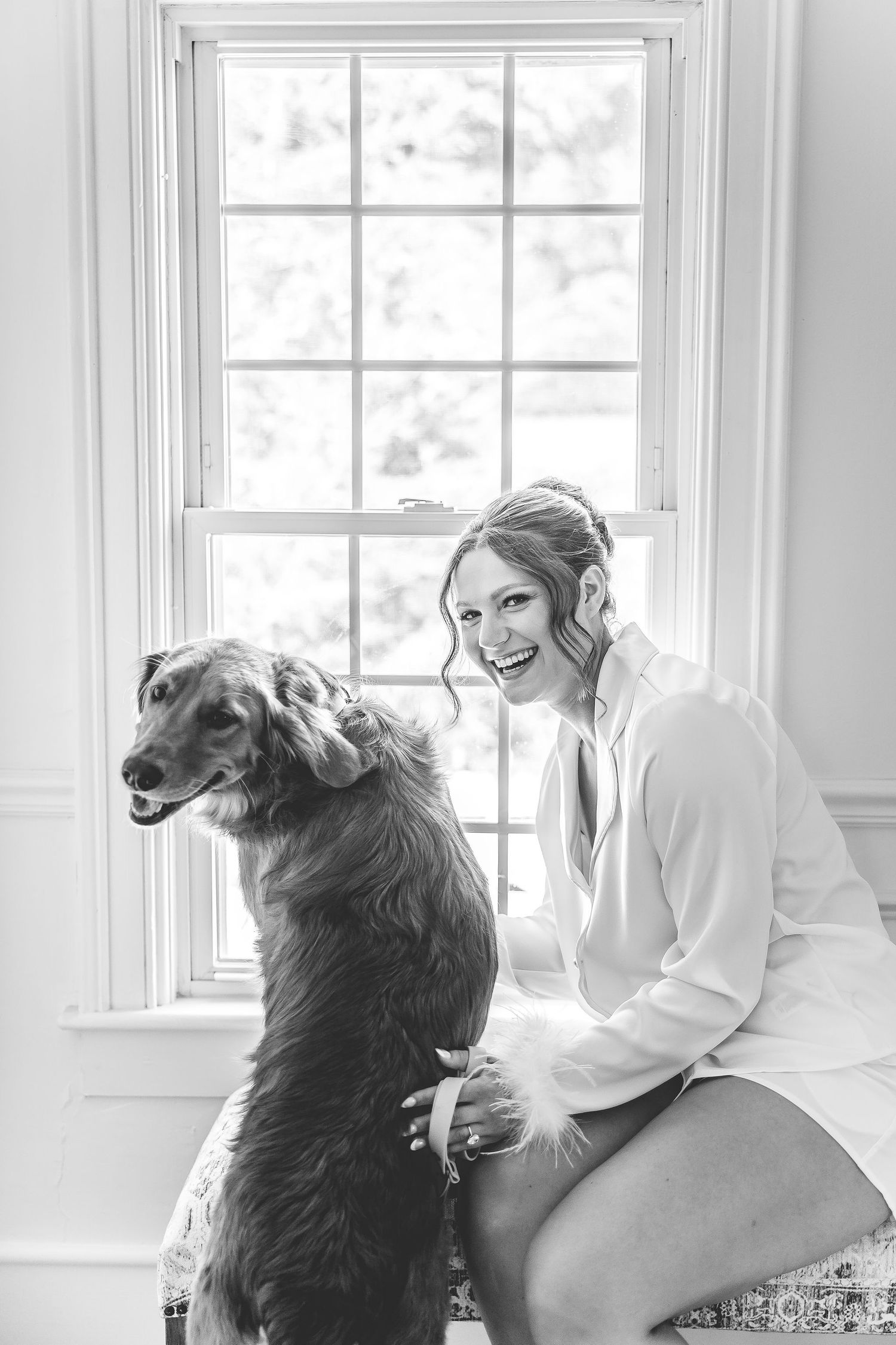 A black and white portrait by a window showing a tender moment with a large dog.