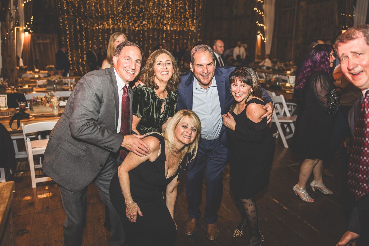 Party guests celebrating and posing for photos in rustic barn venue with wooden walls.