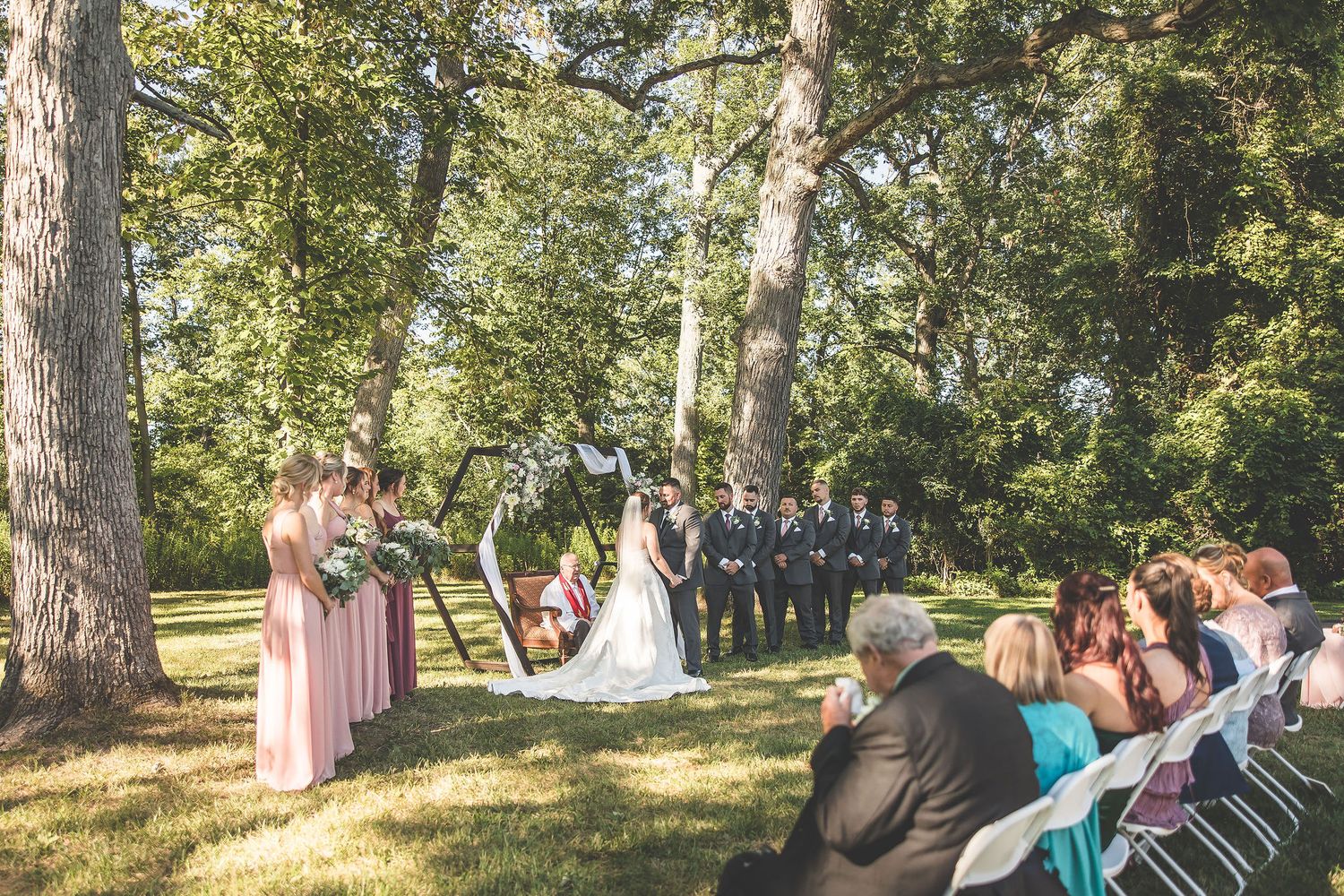 Panoramic view of wedding ceremony setup with white chairs in wooded setting.