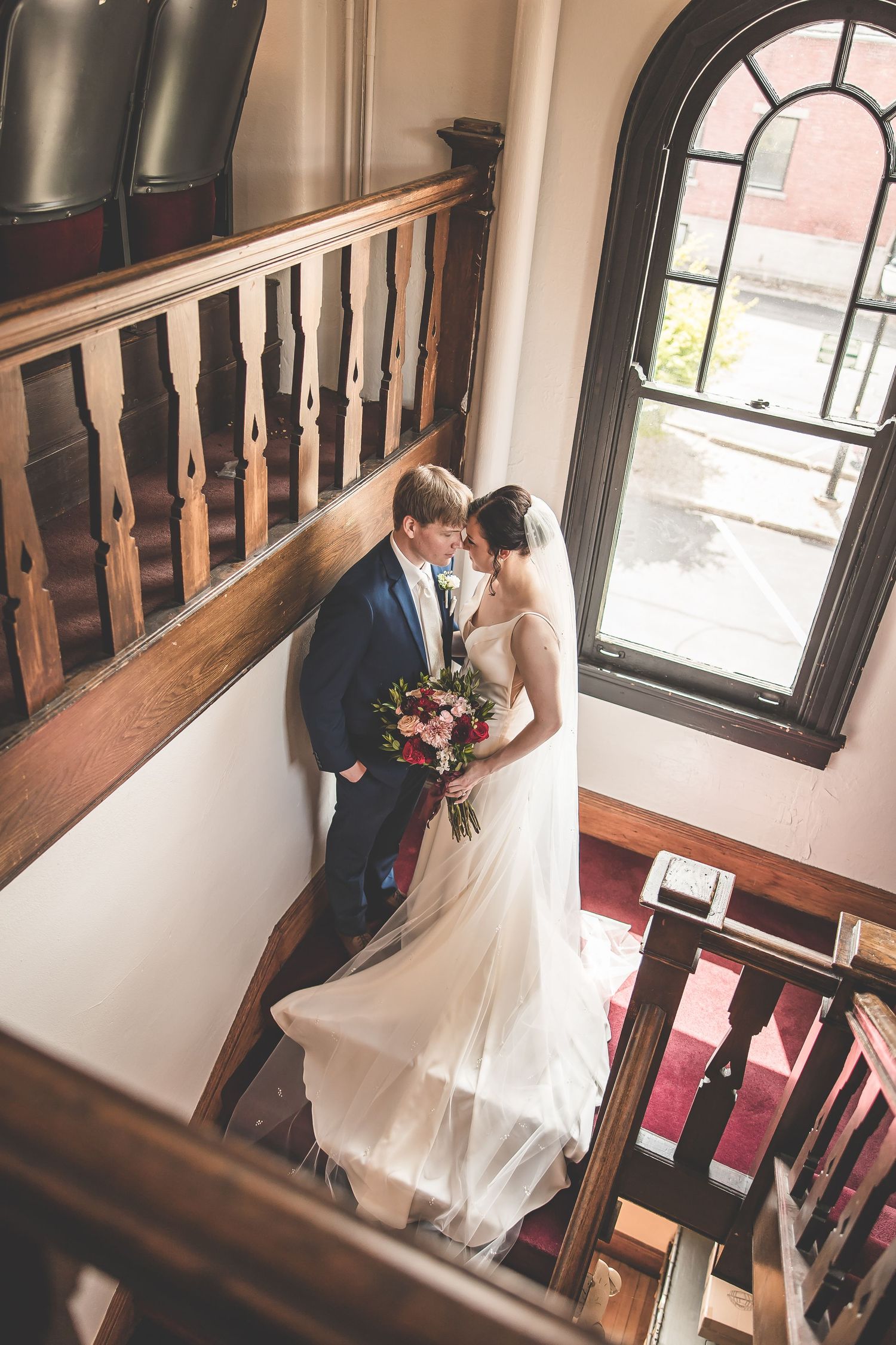 Elegant staircase scene in venue with arched windows and natural lighting.