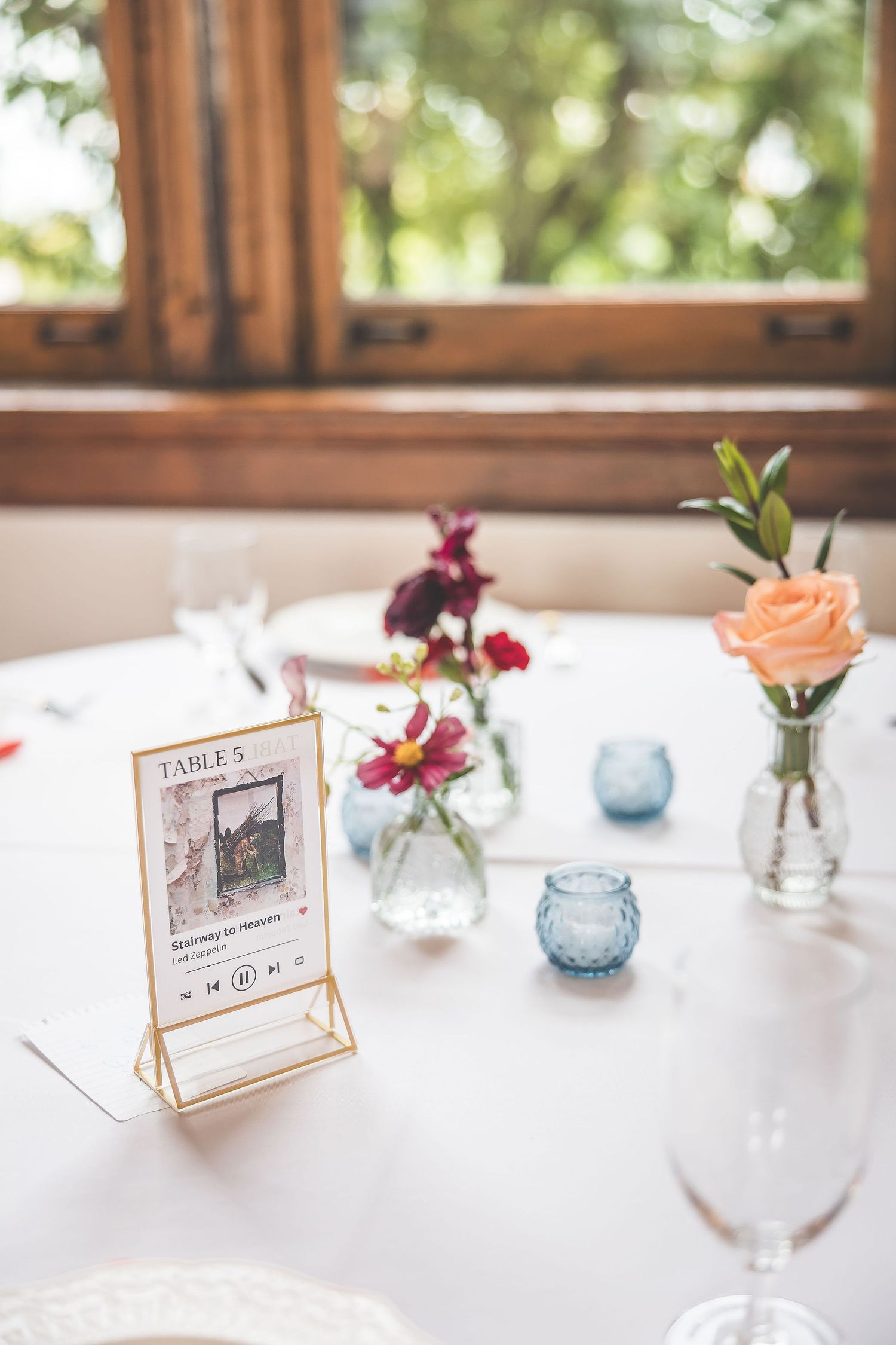 Elegant table settings with framed table numbers and mixed floral arrangements in blue glass vases.