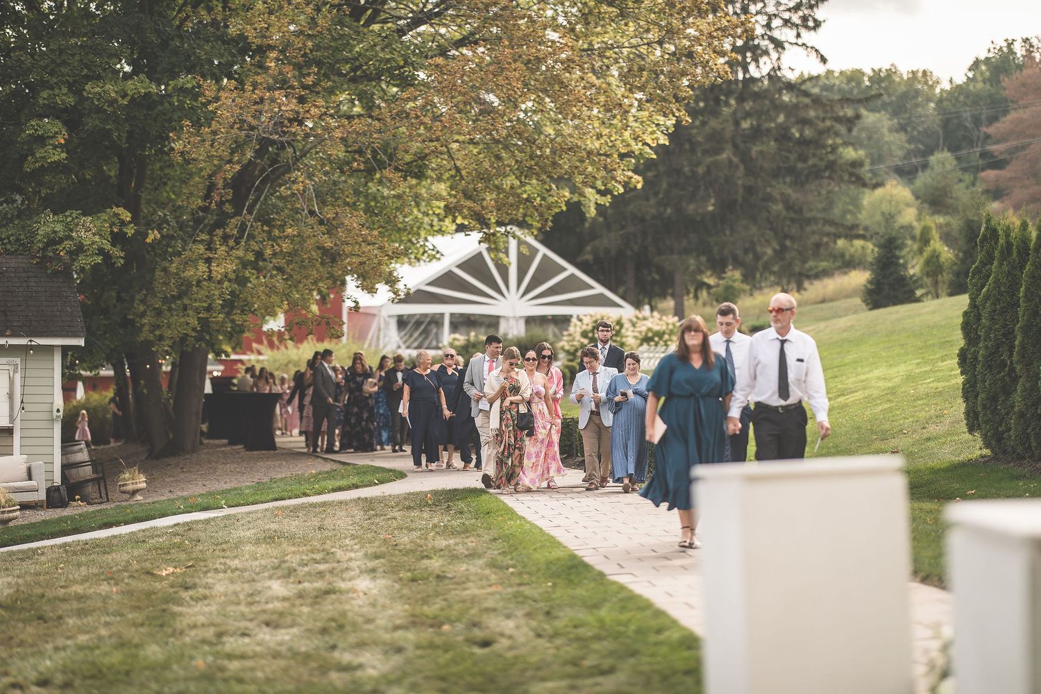 Wedding guests gather outdoors on a scenic hillside path during an autumn ceremony.