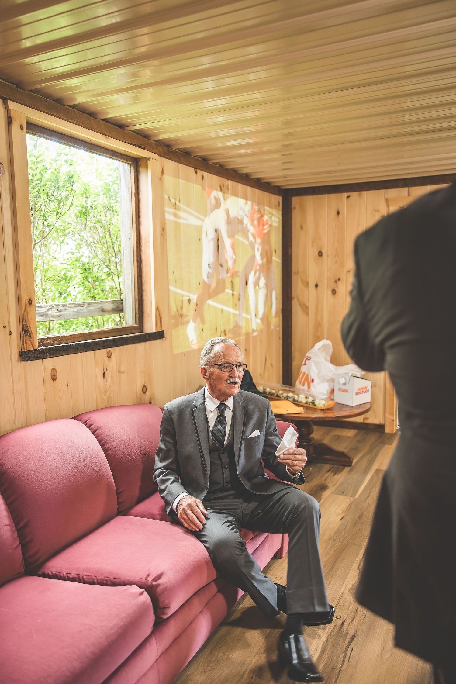 Elegant man in grey suit relaxing on pink couch in wood-paneled room.