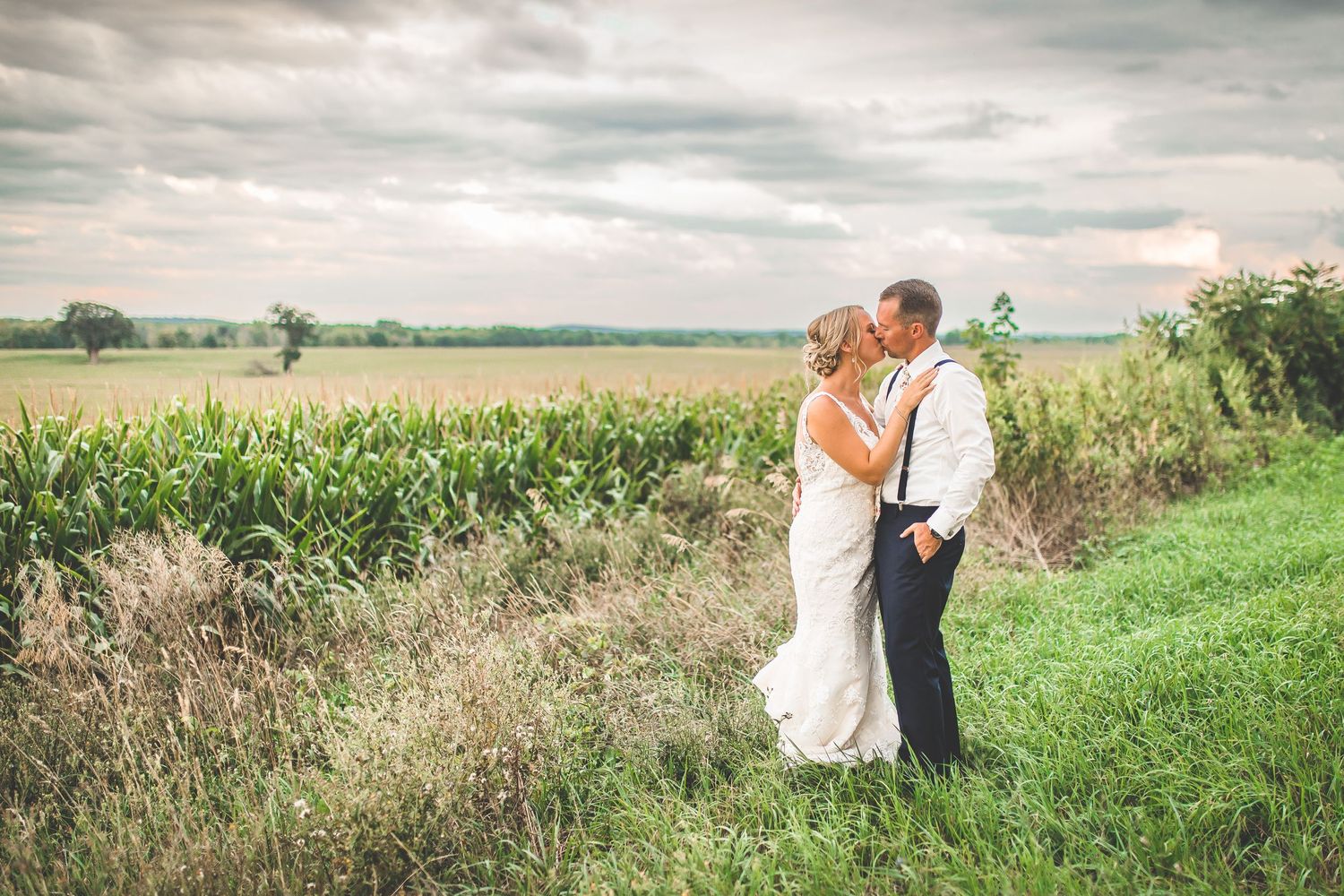 Wedding couple embracing in a scenic field with corn stalks and cloudy skies.