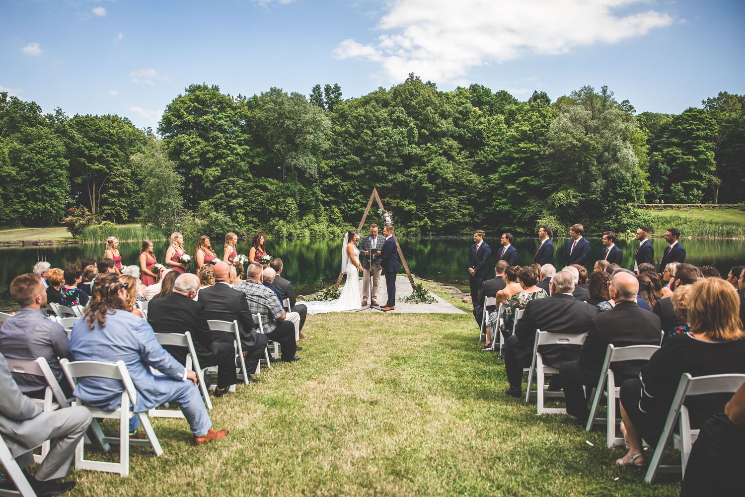 Wide angle view of outdoor wedding ceremony setup with rows of white chairs on grassy hill.