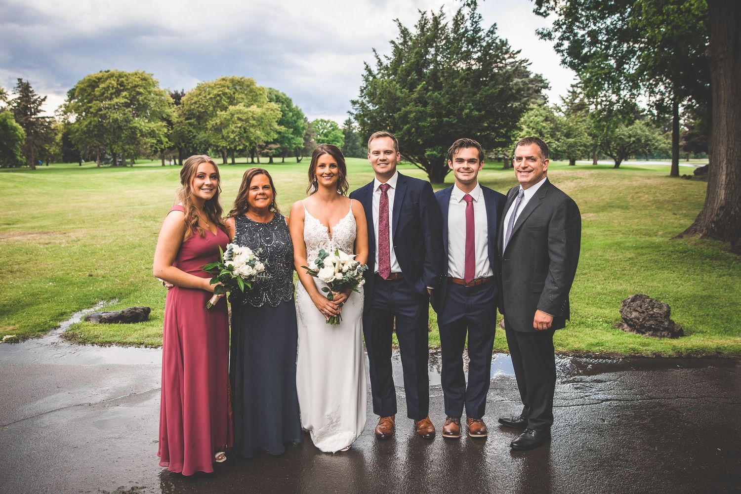 Wedding party poses for photos on cloudy day with green landscape.