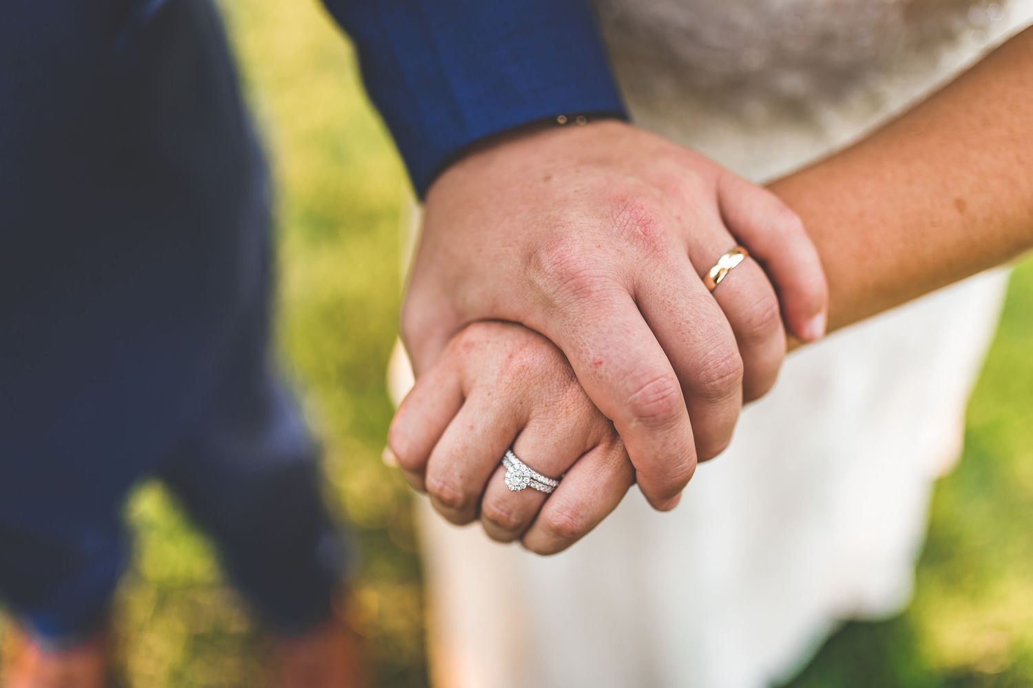 Close-up of couple holding hands during outdoor wedding photoshoot.