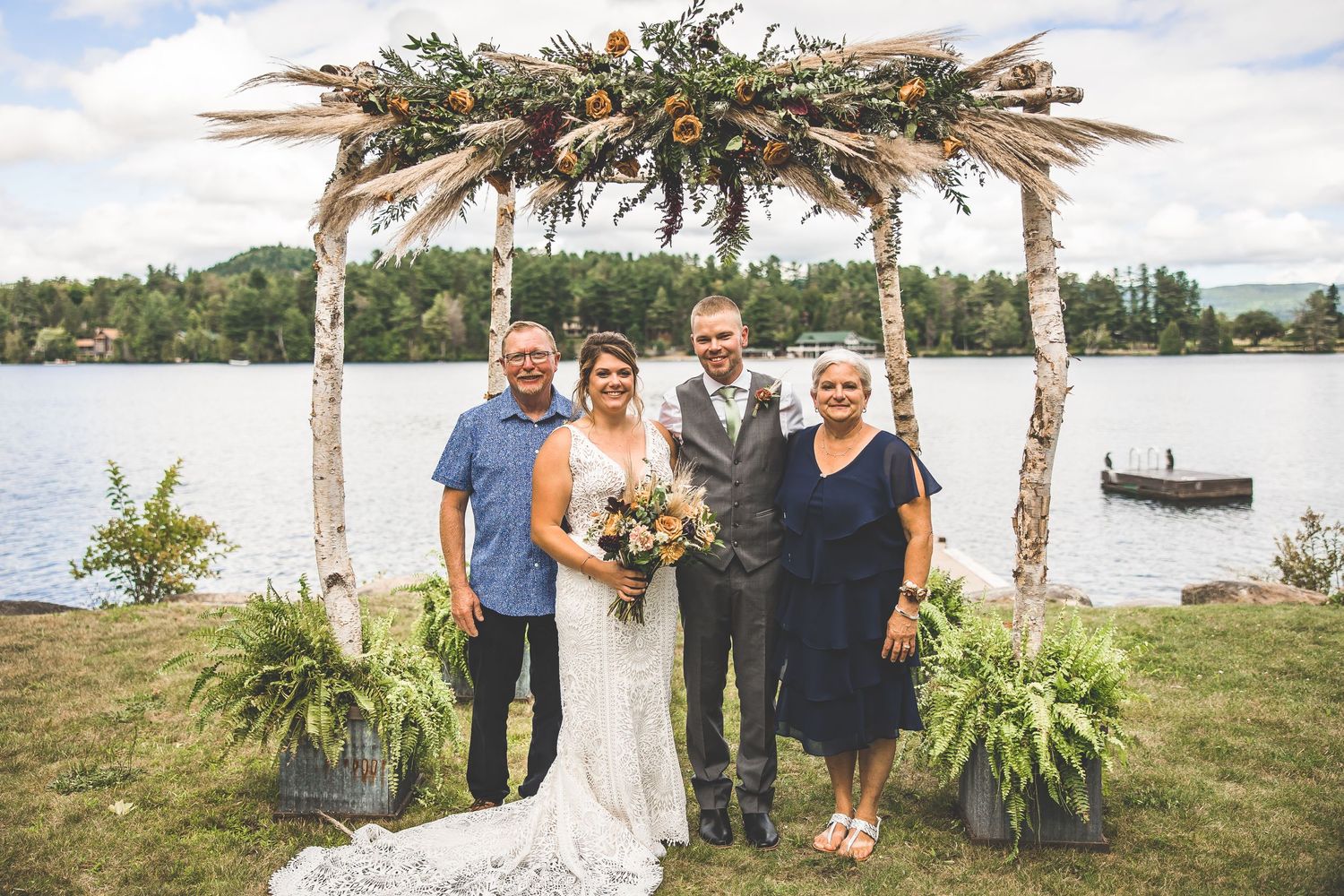 Waterfront wedding ceremony setup with birch branch arch and natural decorations.