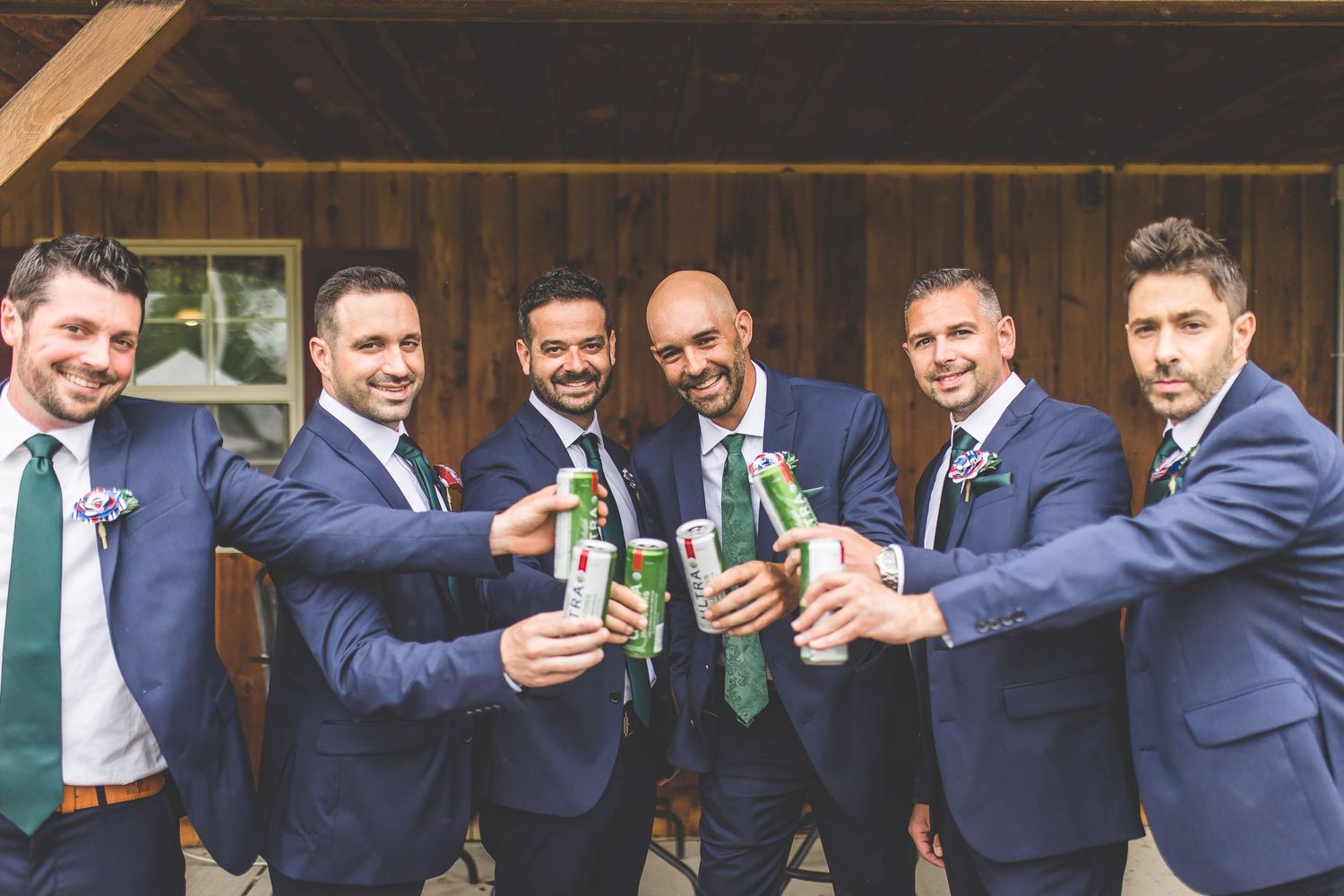 Wedding party toasts with drinks while wearing coordinated navy suits and green ties.