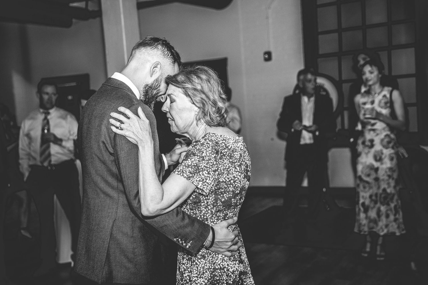 Black and white photo of couples slow dancing at an indoor reception.