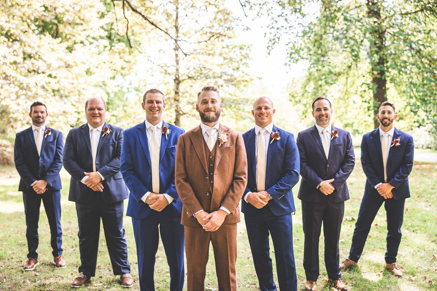 Groomsmen in navy suits and brown accents pose casually outdoors.