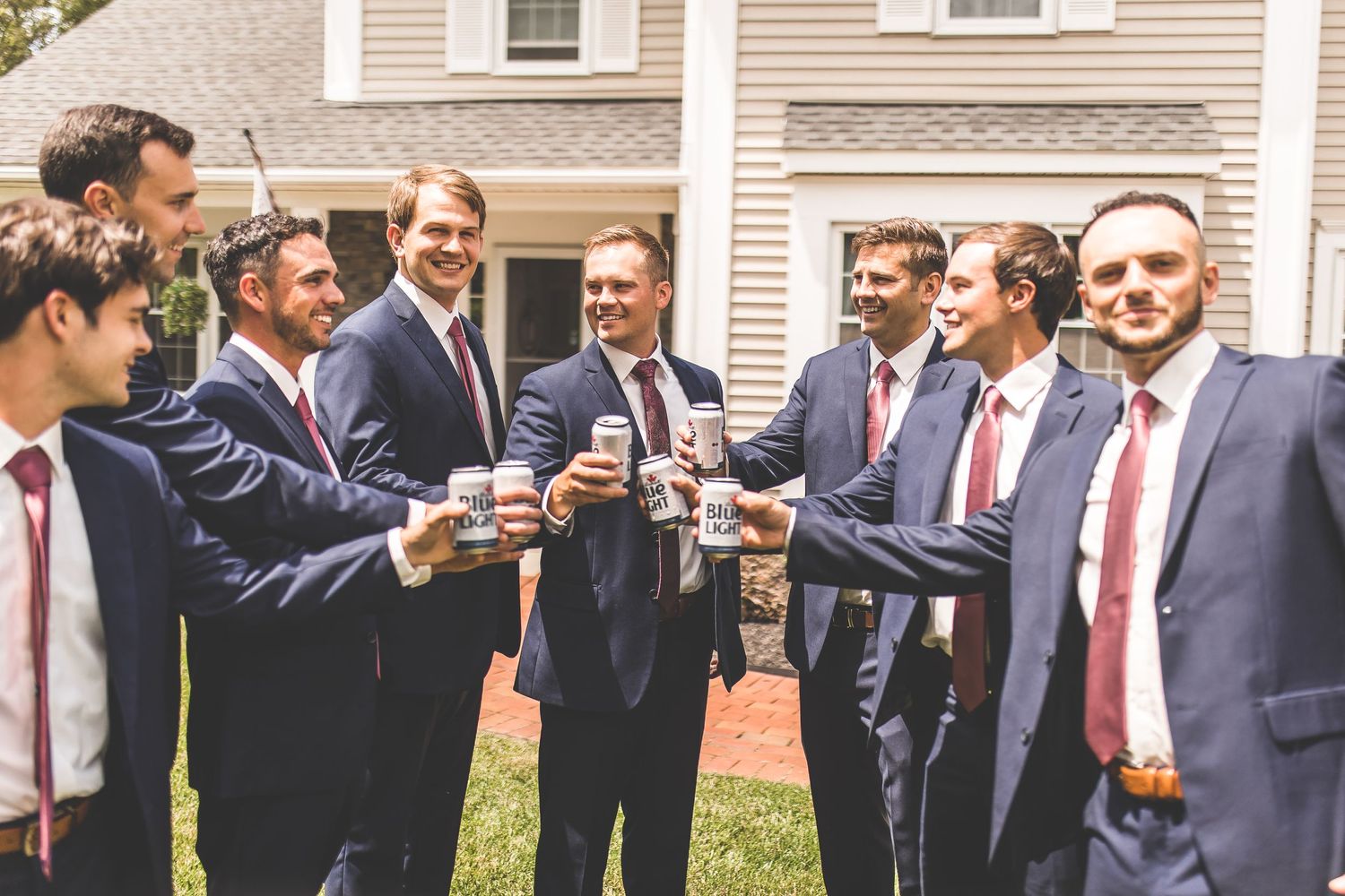 Group of men in suits gathered outdoors in front of a white house.