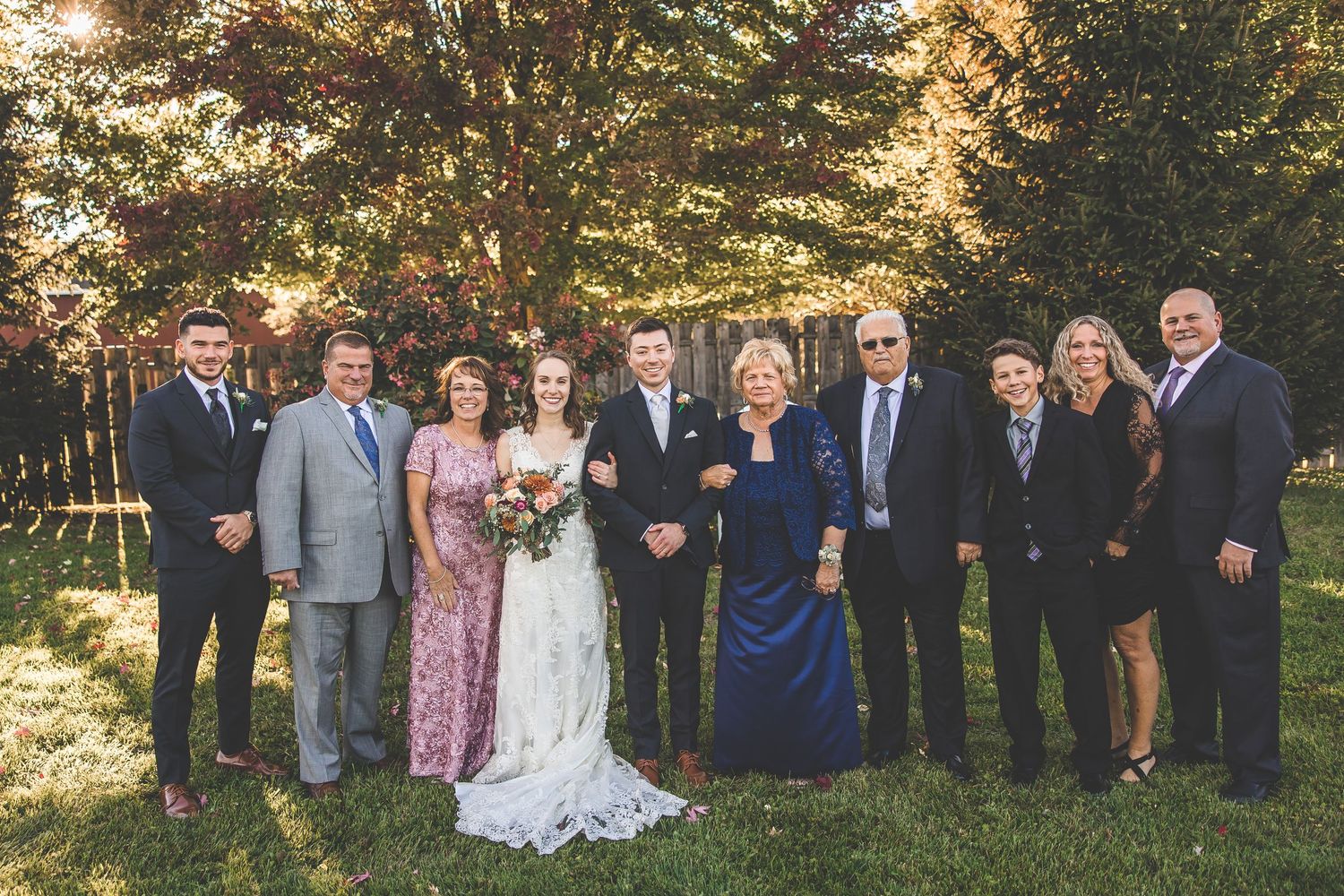 Wedding party and family members gather for formal group photo in autumn setting.