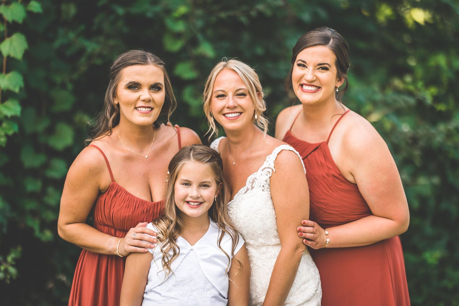 Wedding party members smile and embrace while wearing coordinating rust and white attire.