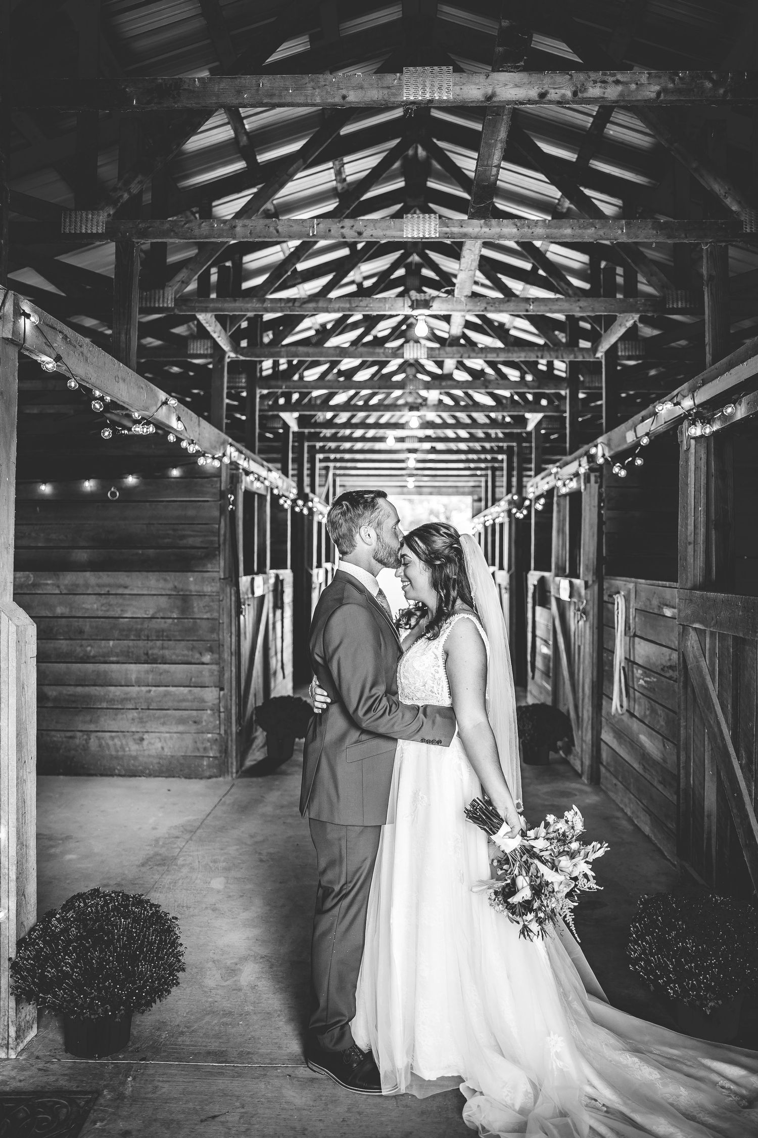 Black and white wedding photos in rustic barn setting with dramatic lighting and wooden architecture.