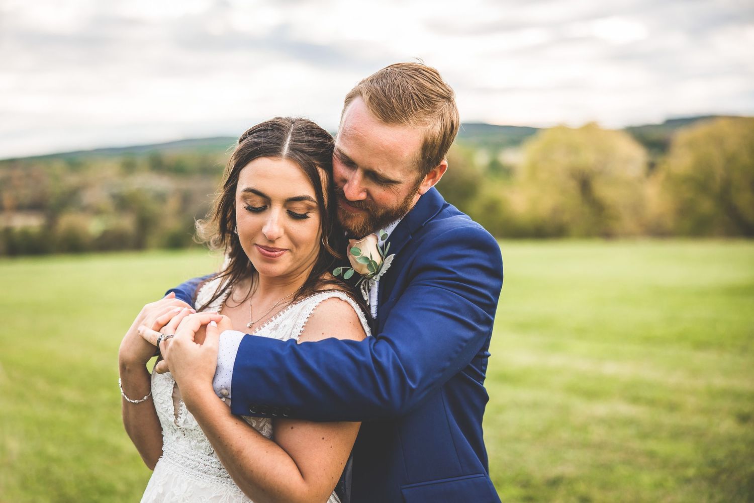 Romantic wedding couple embraces while dancing in a sunlit meadow surrounded by rolling hills.