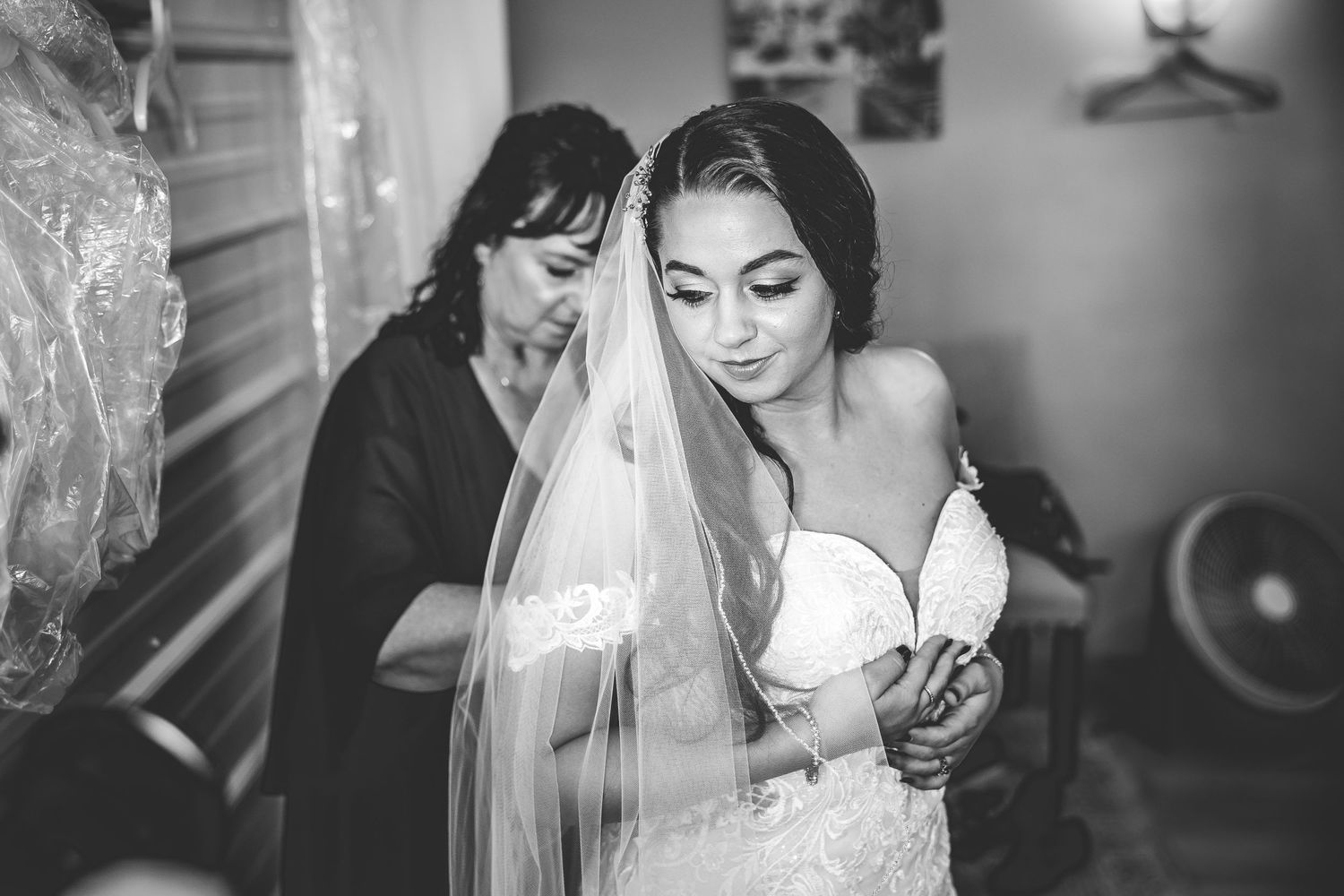 Black and white photo of bridal preparation with veil and dress fitting.