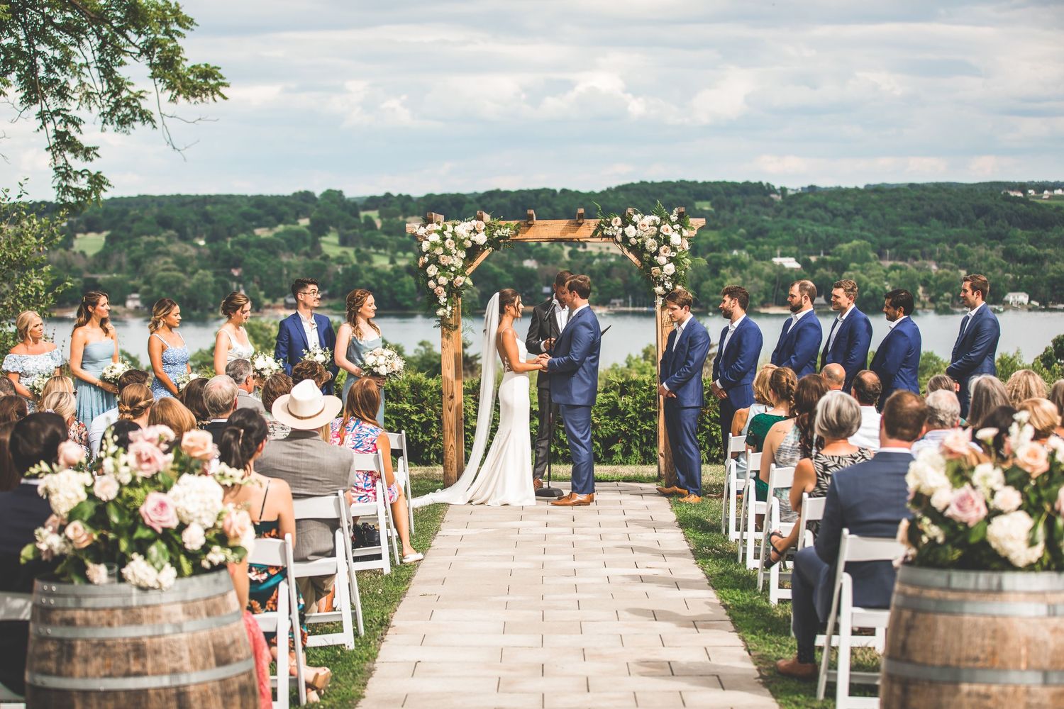 Outdoor wedding ceremony setup with wooden barrels and white chairs against mountain backdrop.