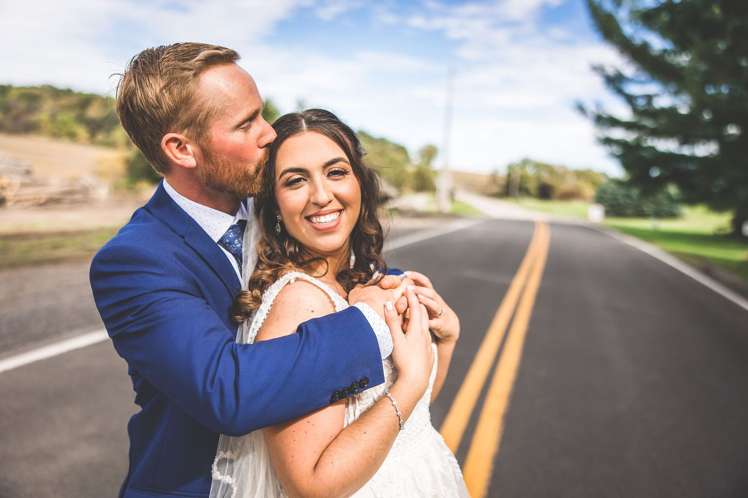 Romantic wedding portraits taken on a paved road with blue sky and trees in the background.