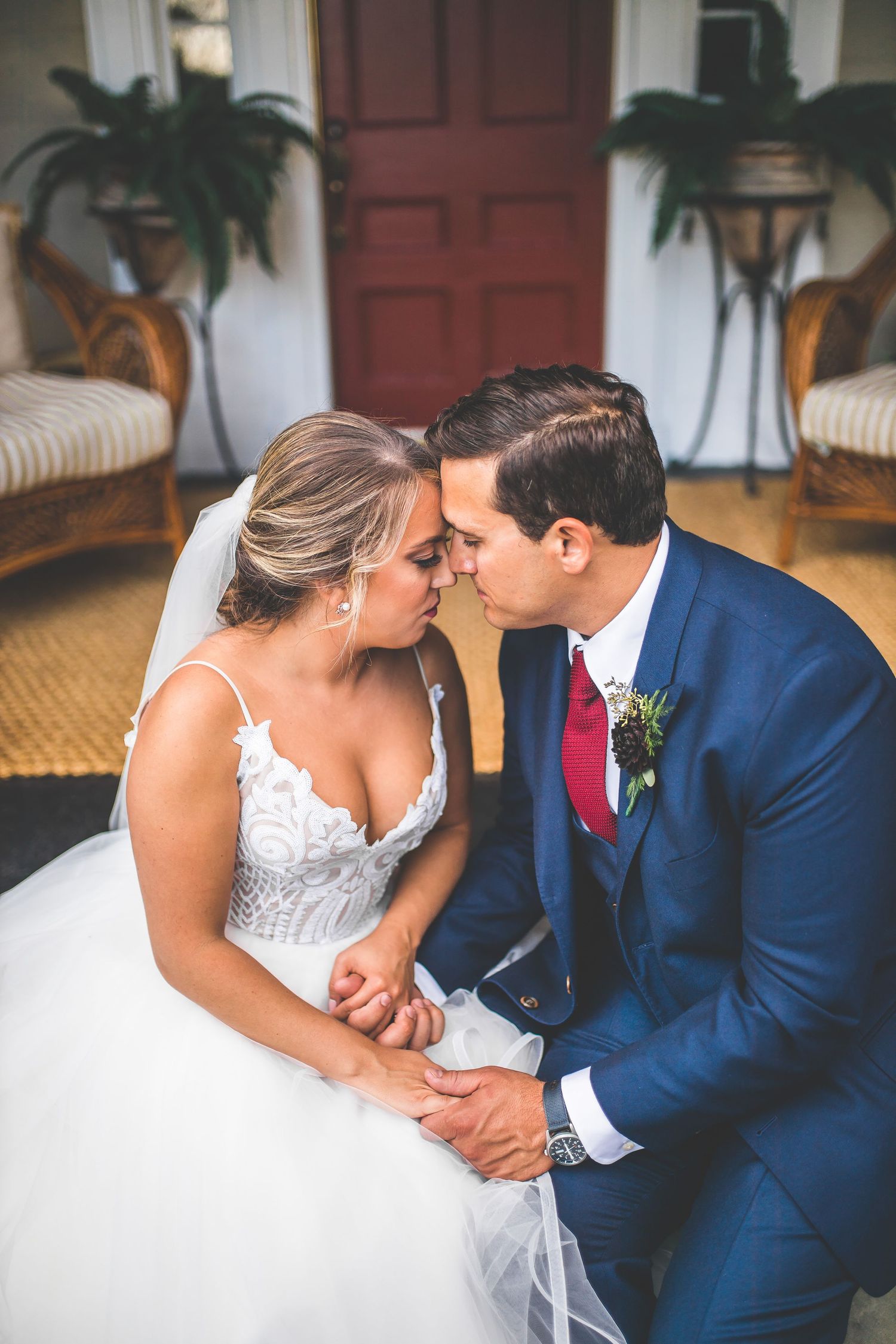 An intimate wedding portrait on a porch with wicker chairs and potted plants framing the scene.