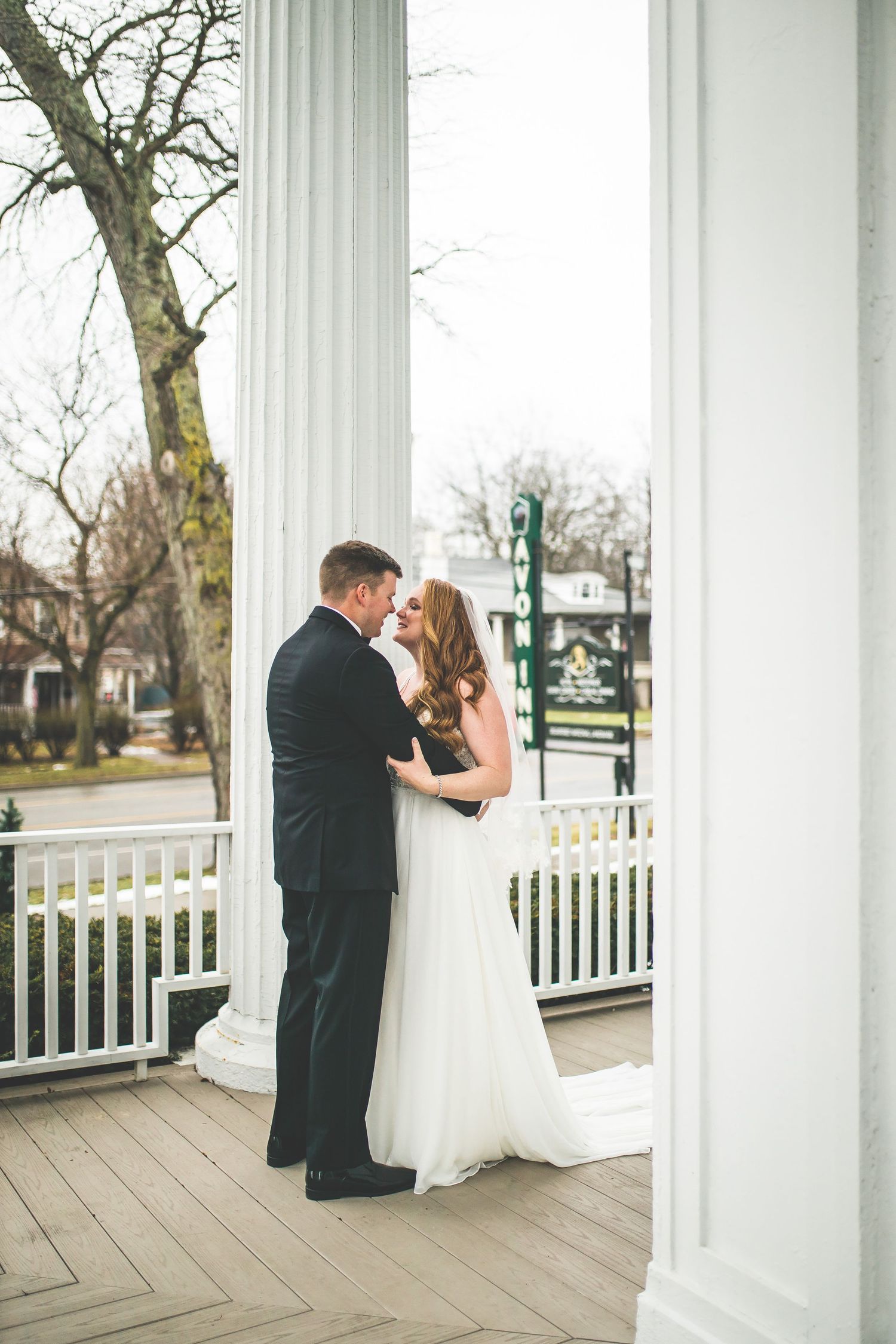 A romantic first look between newlyweds on a columned porch with white railings.