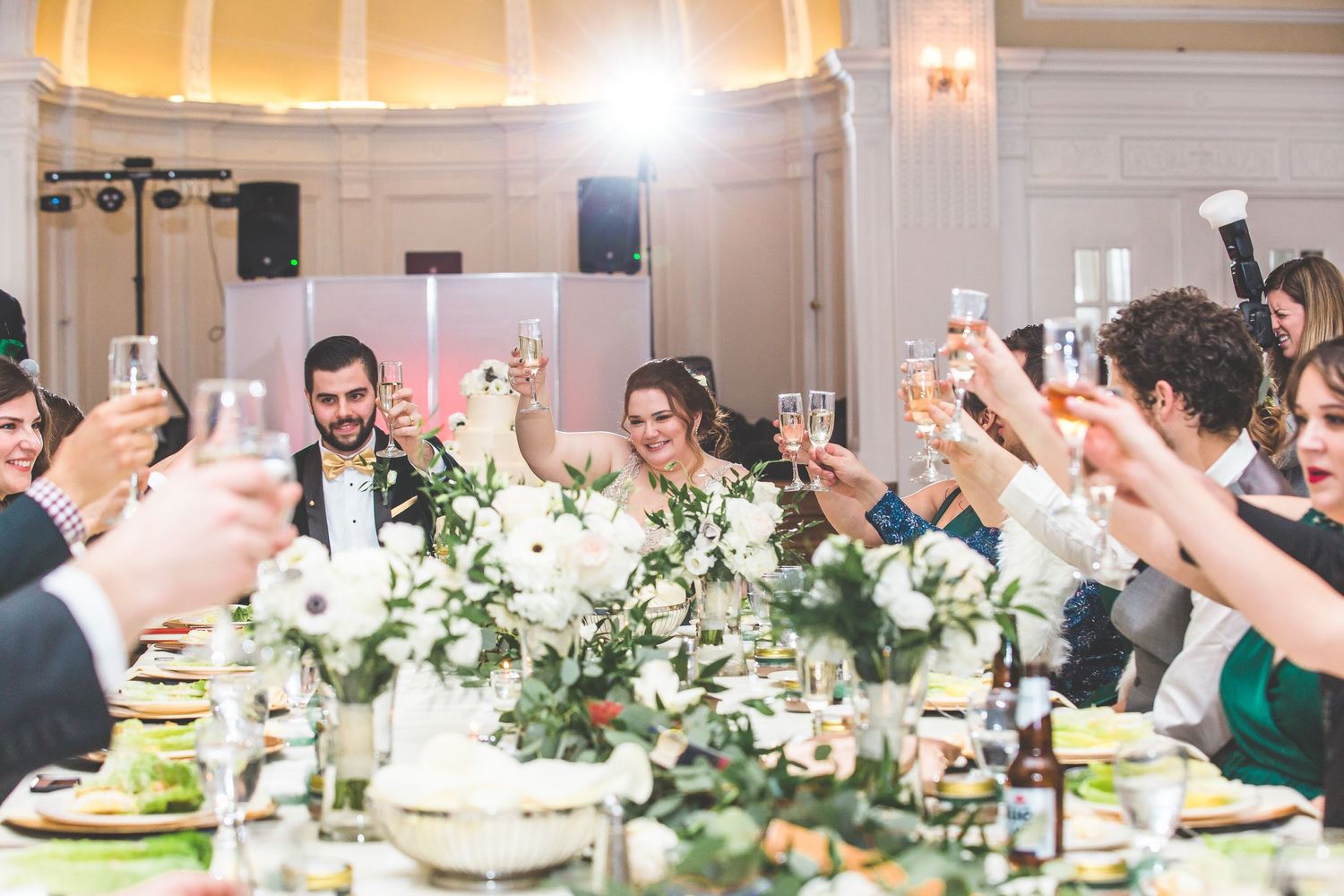 Long banquet tables decorated with white floral arrangements and greenery in an elegant reception hall.