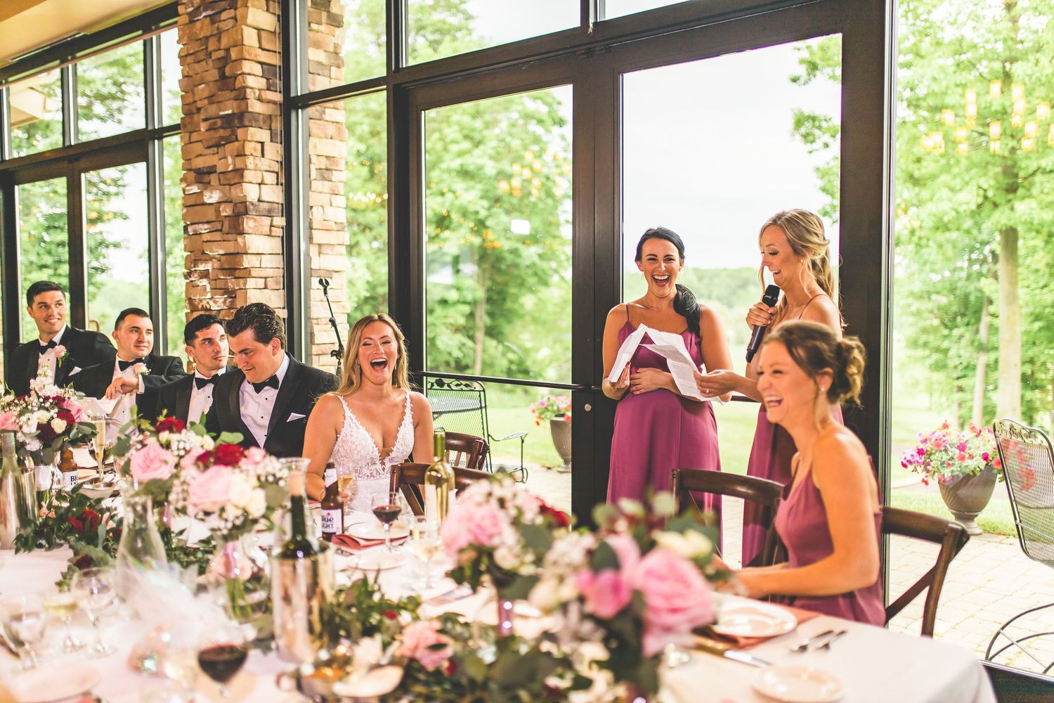 Wedding reception table decorated with pink flowers as guests gather for celebration.