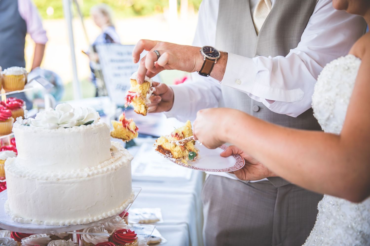 Close-up of hands cutting into a white tiered wedding cake during reception.