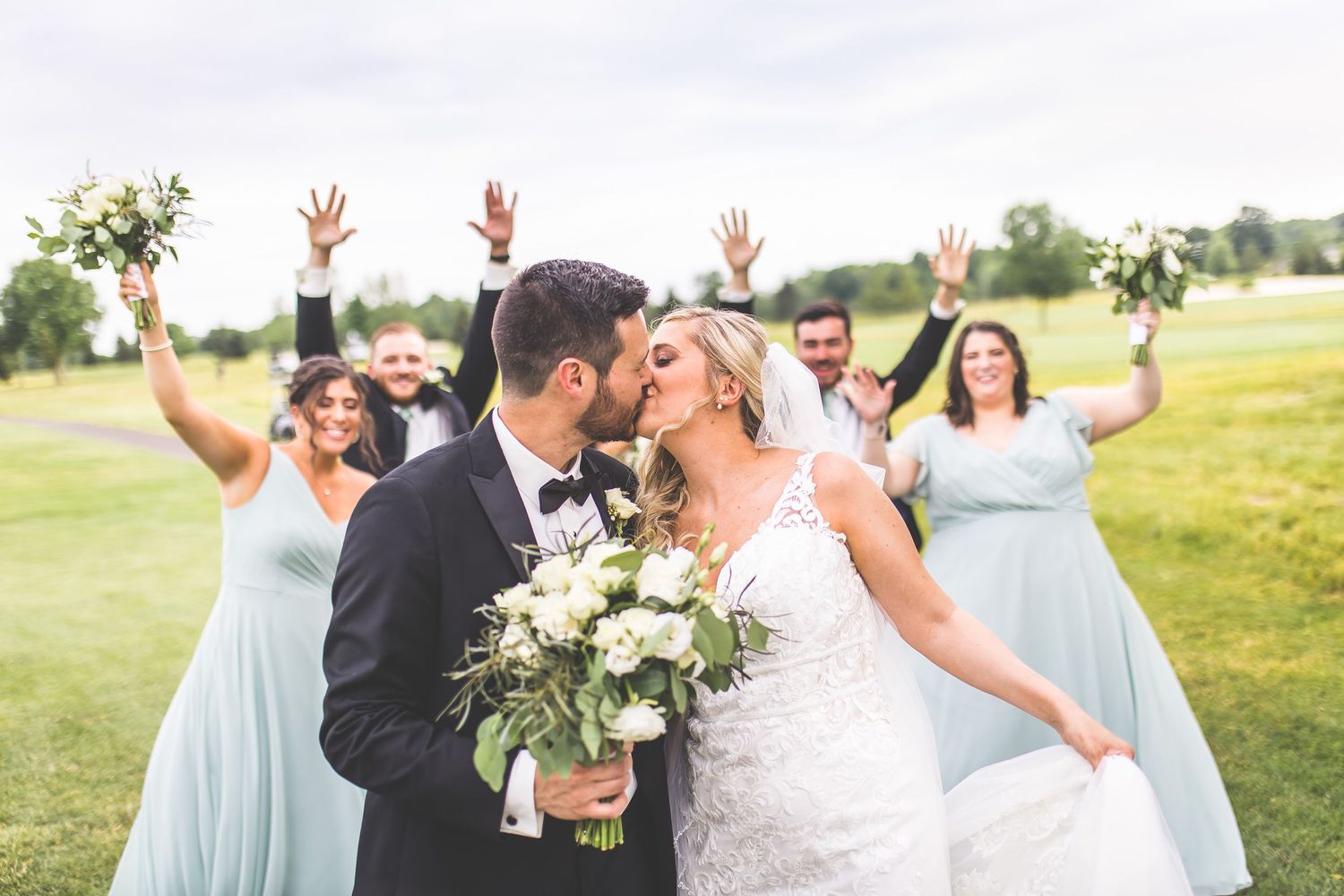 Wedding party in light blue dresses poses outdoors with white floral bouquets.