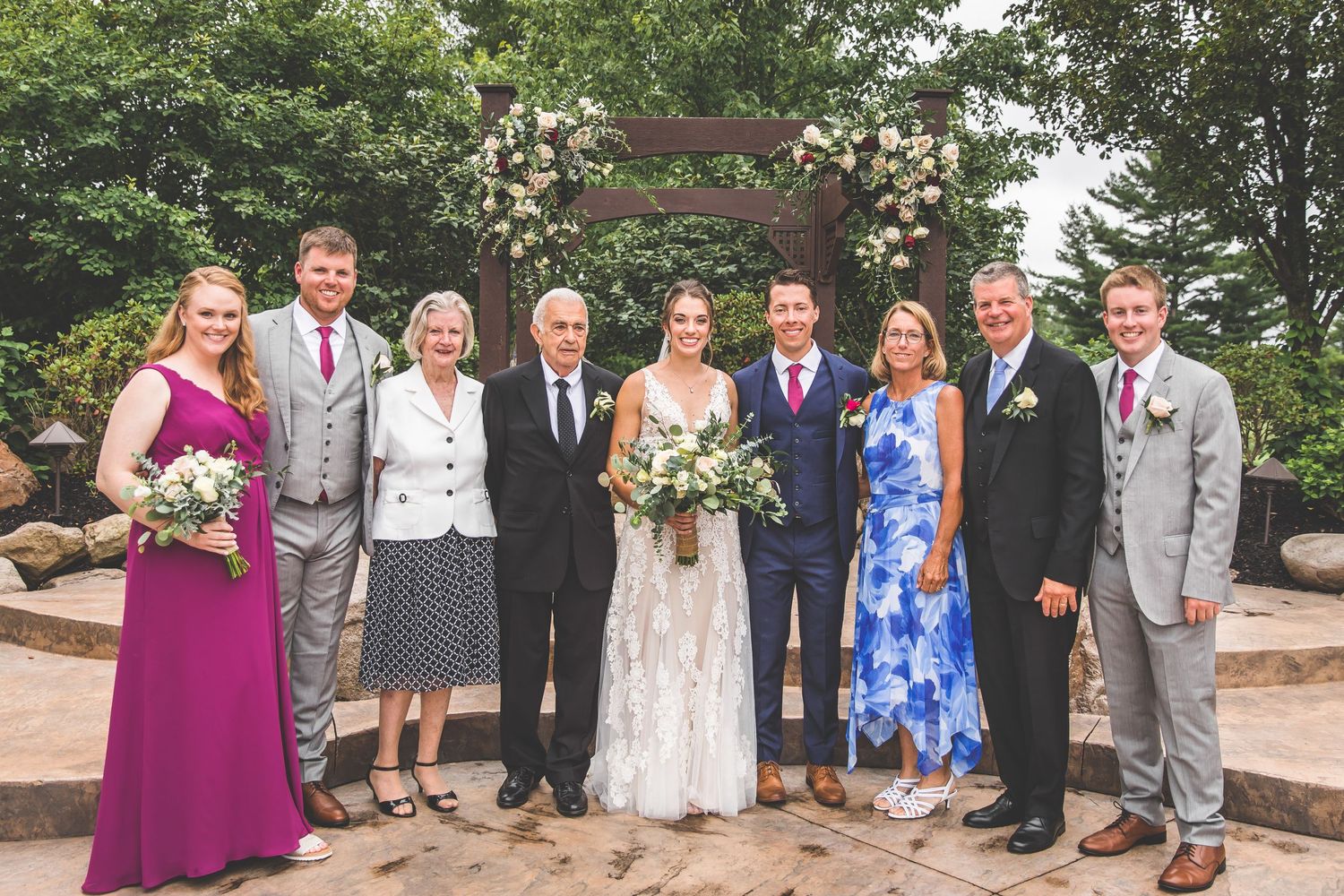 Large wedding party group photo with bridesmaids in purple dresses and groomsmen in grey suits.