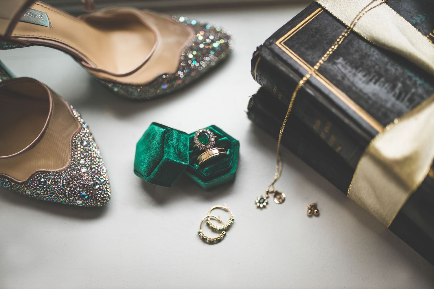 Close-up of wedding accessories including sparkly shoes and jewelry on a dark surface.