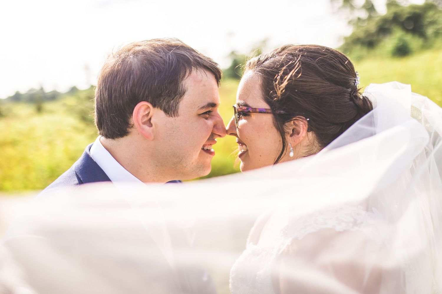 Intimate wedding portrait through white veil in golden sunlight.