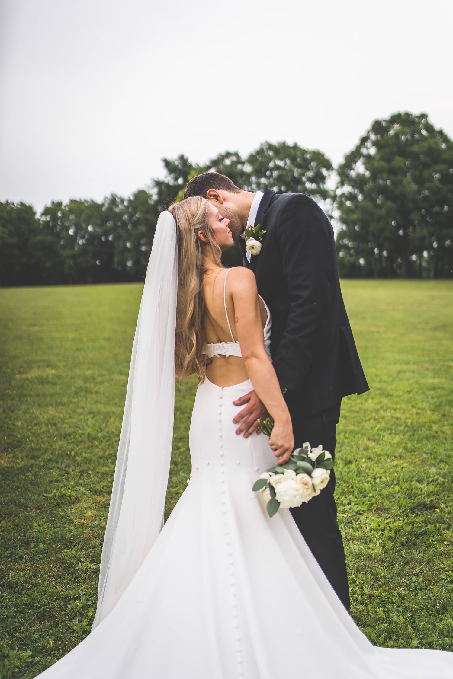 Romantic outdoor wedding portraits with flowing white dress and veil against green landscape.