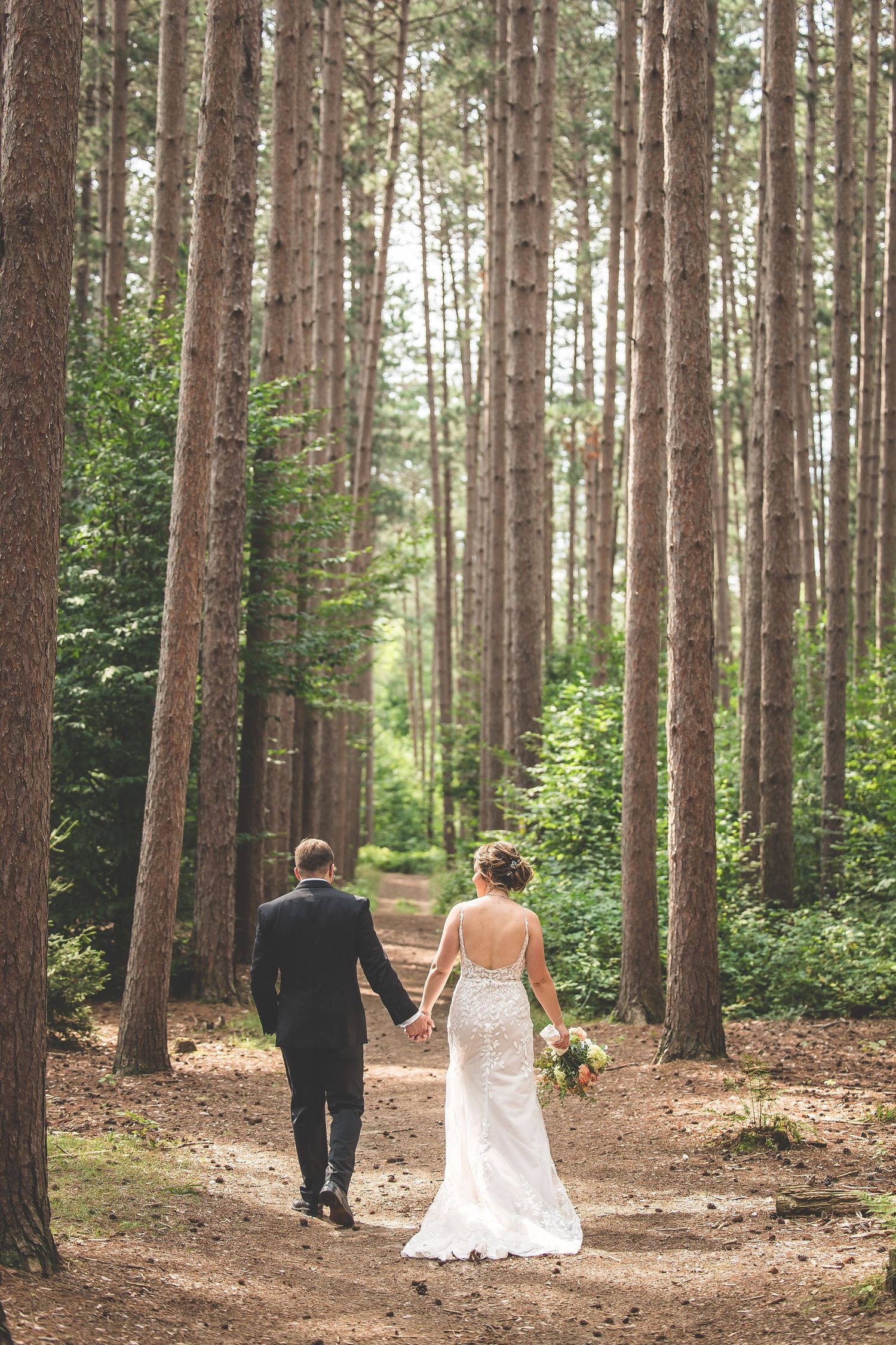 Wedding couple walking hand in hand through a serene pine forest path.