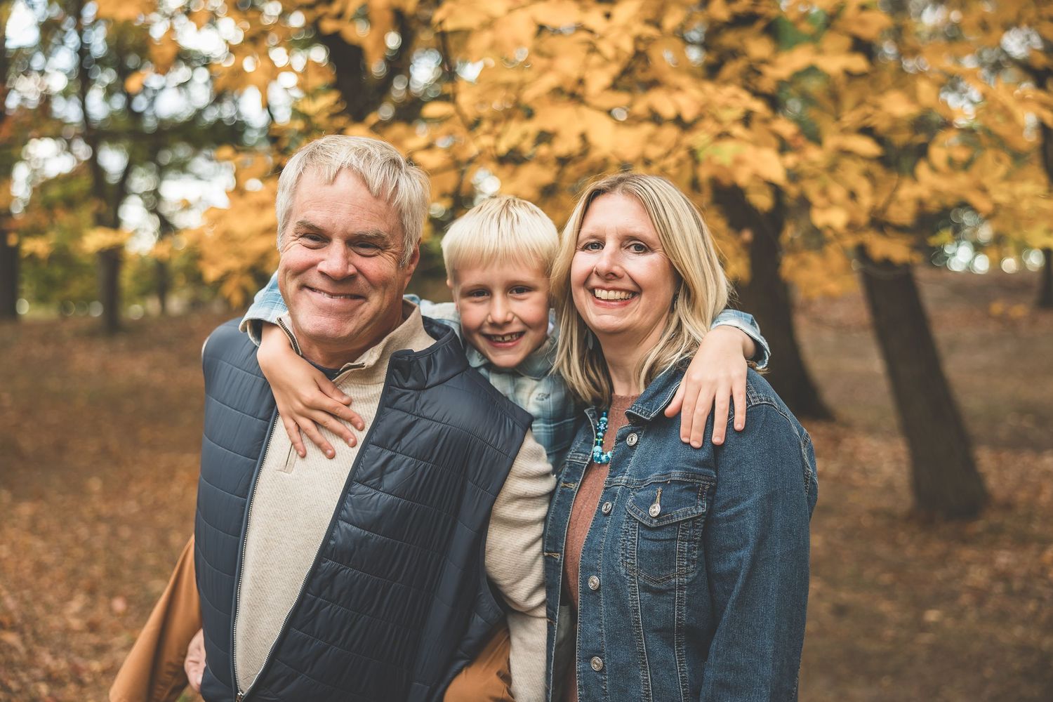 Family group embraces while posing outdoors during autumn with golden leaves in background.