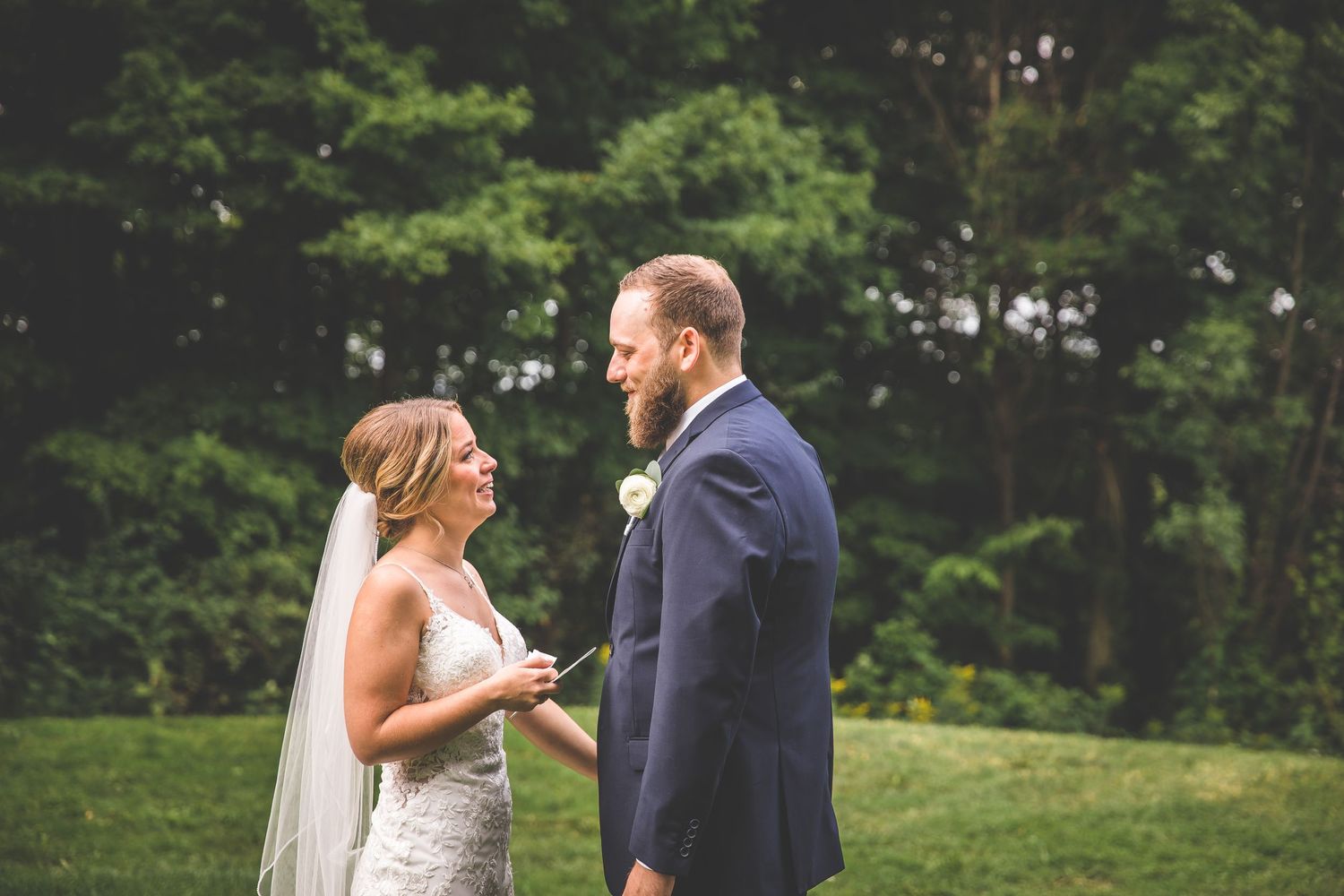 Couple exchanges heartfelt reactions during wedding first look on green hillside.