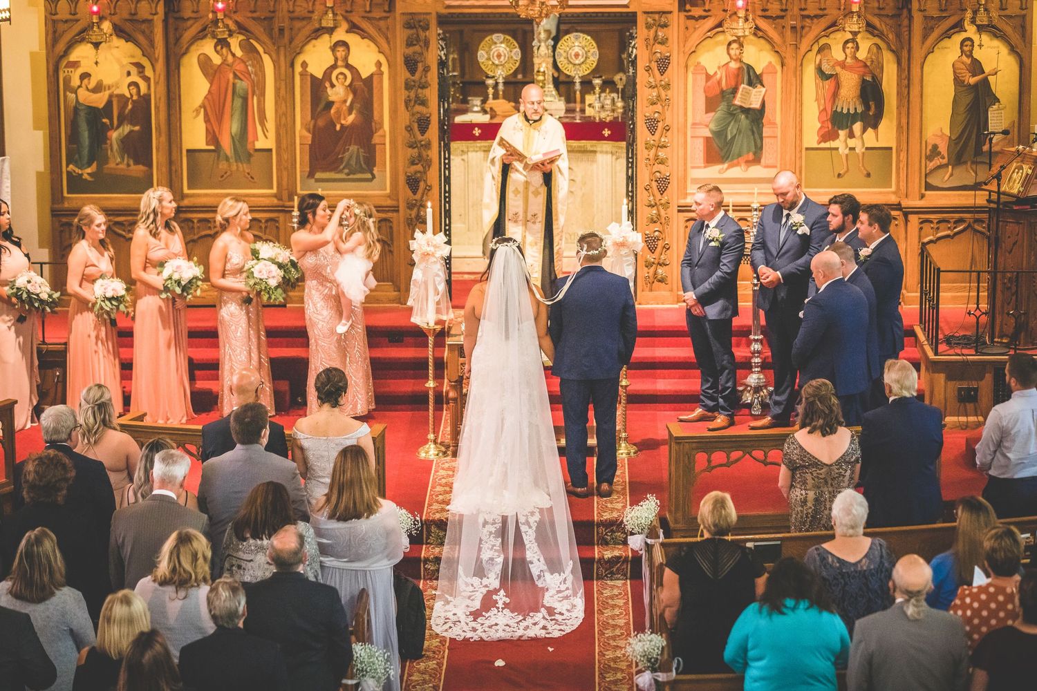 Panoramic shot of a church wedding ceremony with ornate religious artwork and red carpet.