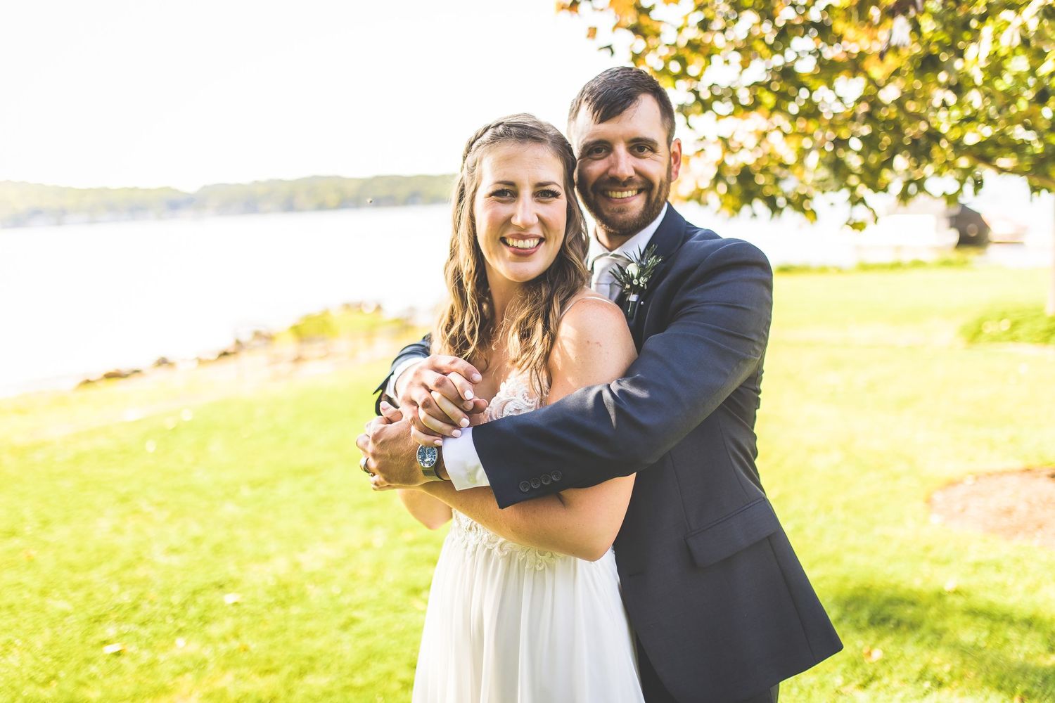 Sun-drenched wedding portrait on a grassy hillside overlooking water.