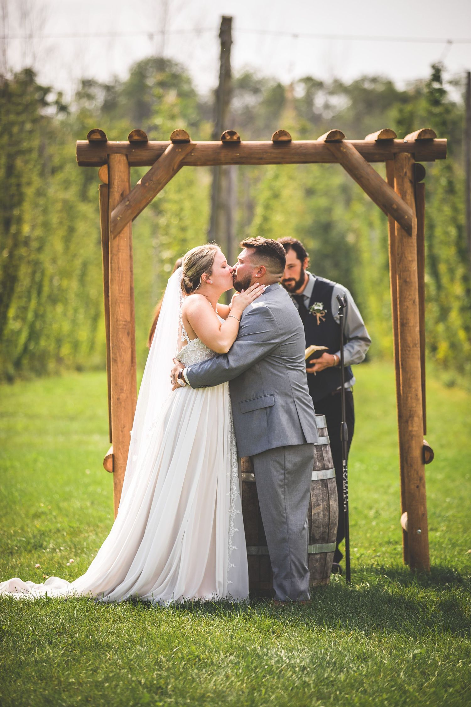 Emotional wedding ceremony moment under wooden pergola with barrel altar in garden setting.