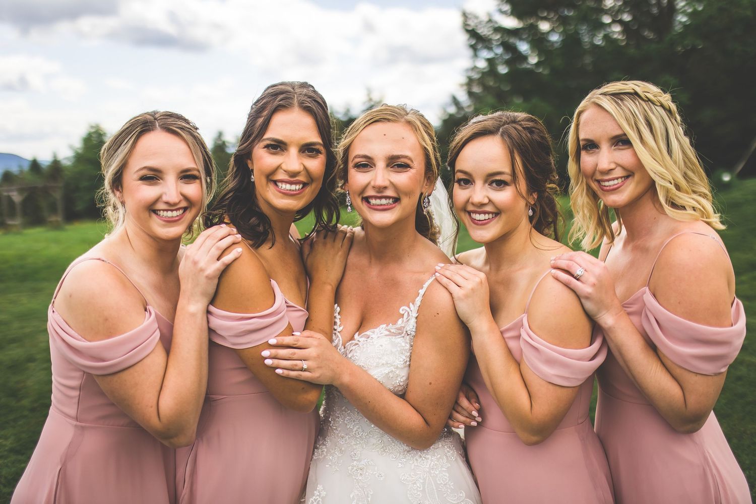 Bridesmaids in pink dresses share intimate moment during outdoor wedding photoshoot.