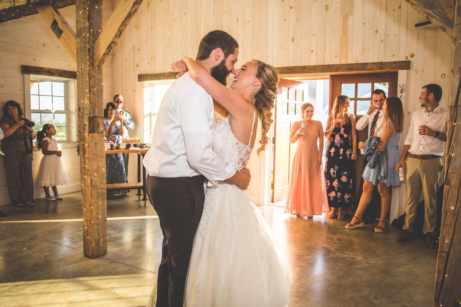 A couple shares their first dance in a rustic barn venue surrounded by wedding guests.