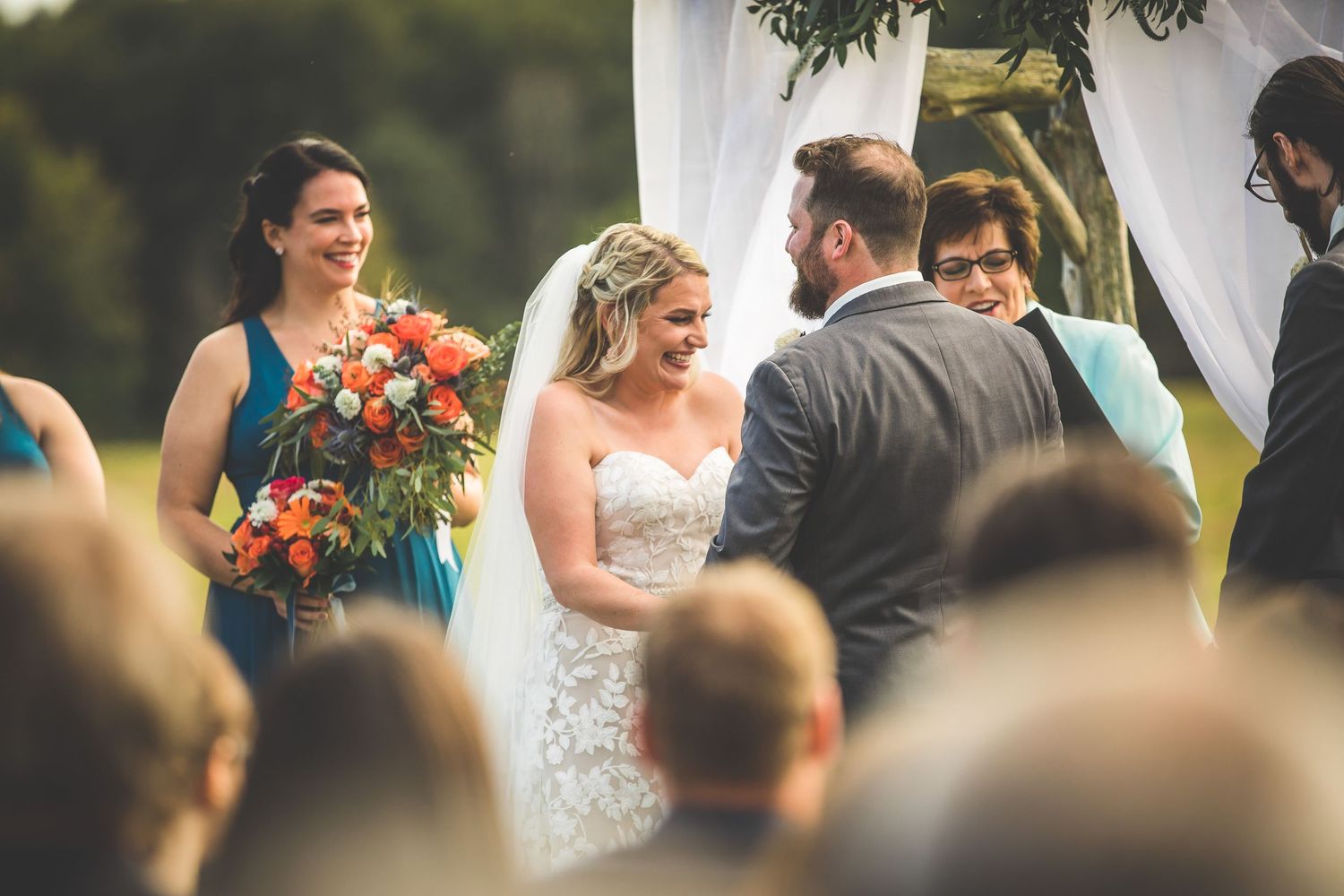 Close-up view of wedding ceremony under a white canopy decorated with vibrant flowers.