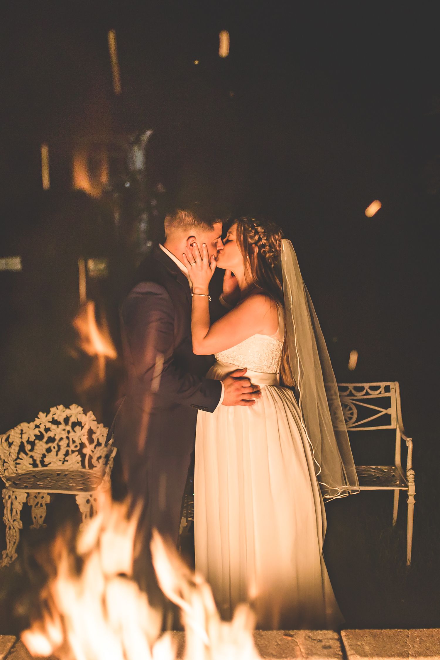 A couple shares an intimate moment by a bonfire during their wedding reception.