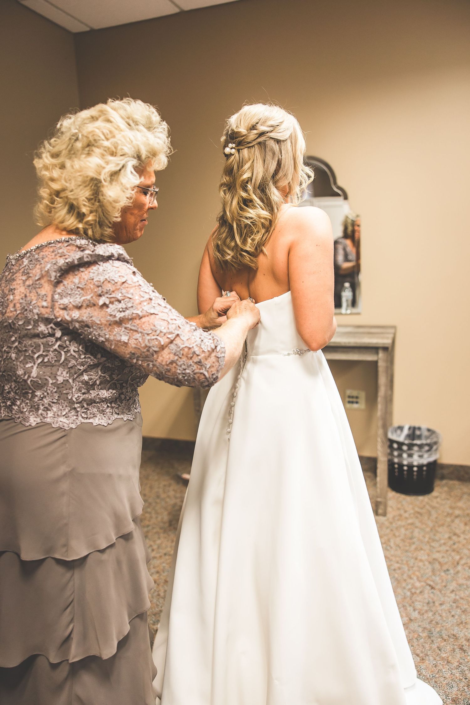 A touching moment of wedding dress preparation captured in warm indoor lighting.