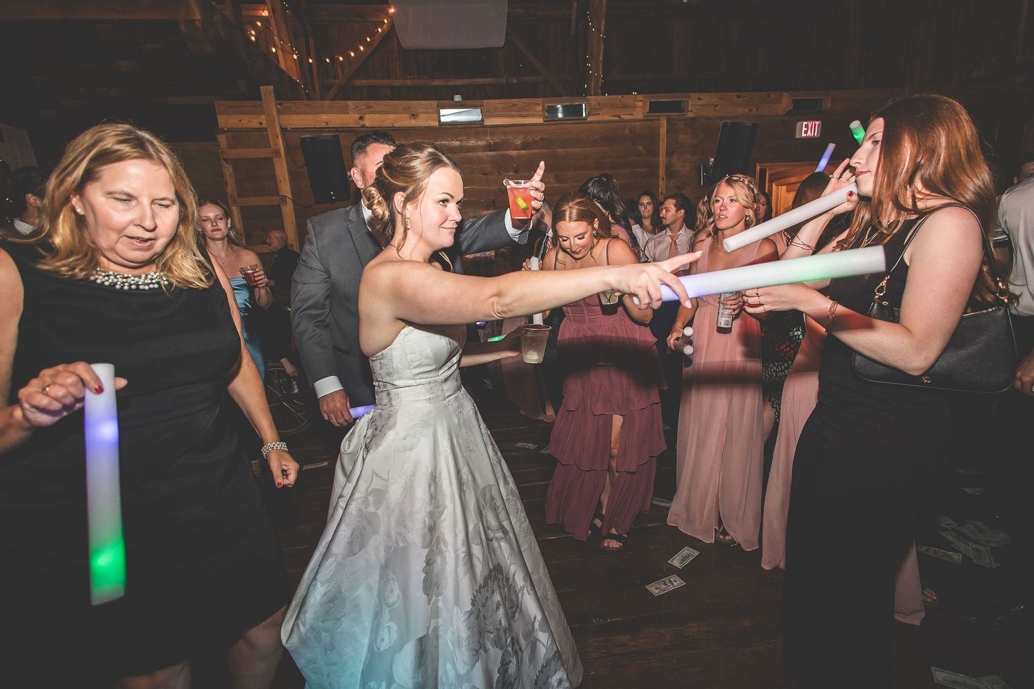 Wedding party dancing in a dimly lit barn with colorful lighting effects.