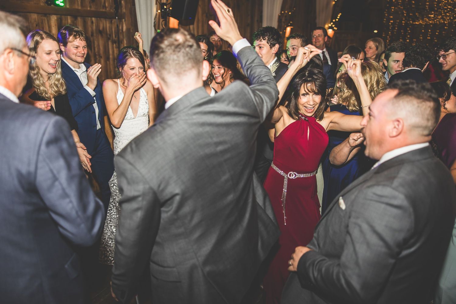 Wedding guests dance and celebrate during reception in rustic barn setting.
